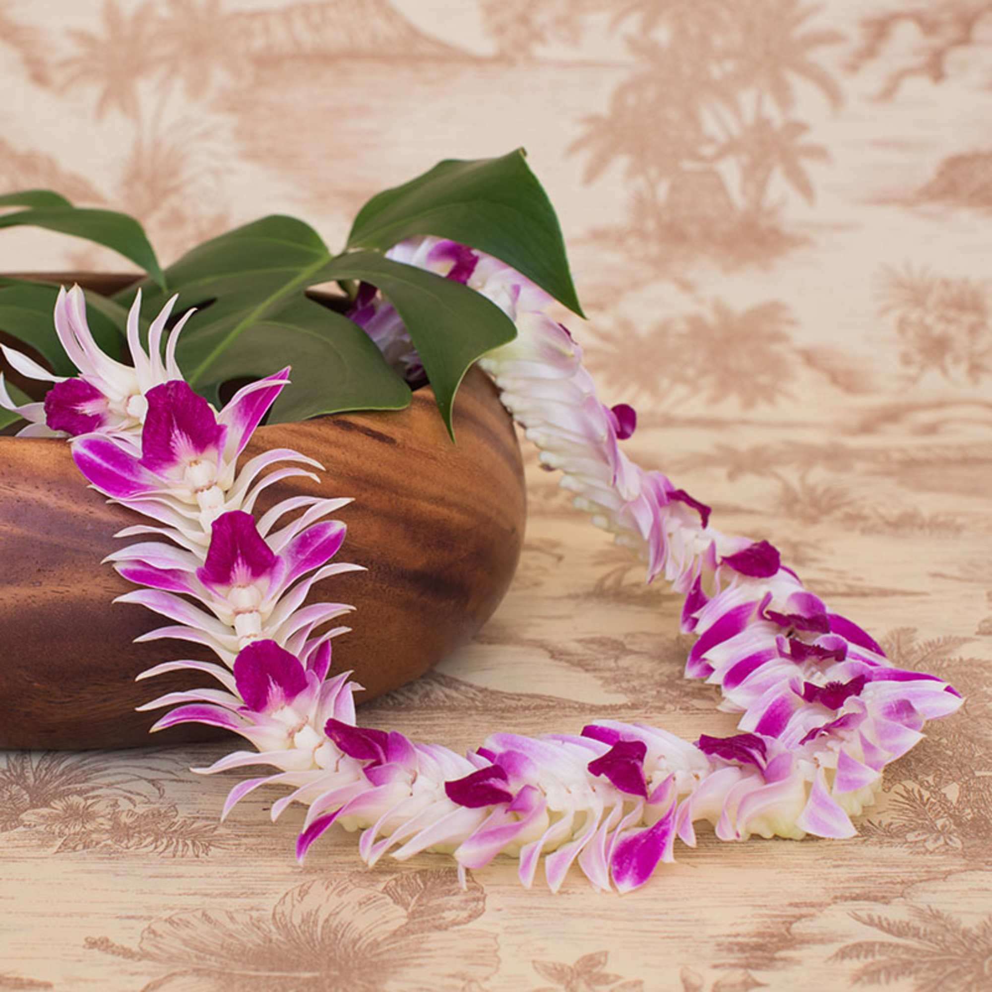 Purple and white orchid lei draped from a wood bowl with large tropical leaves