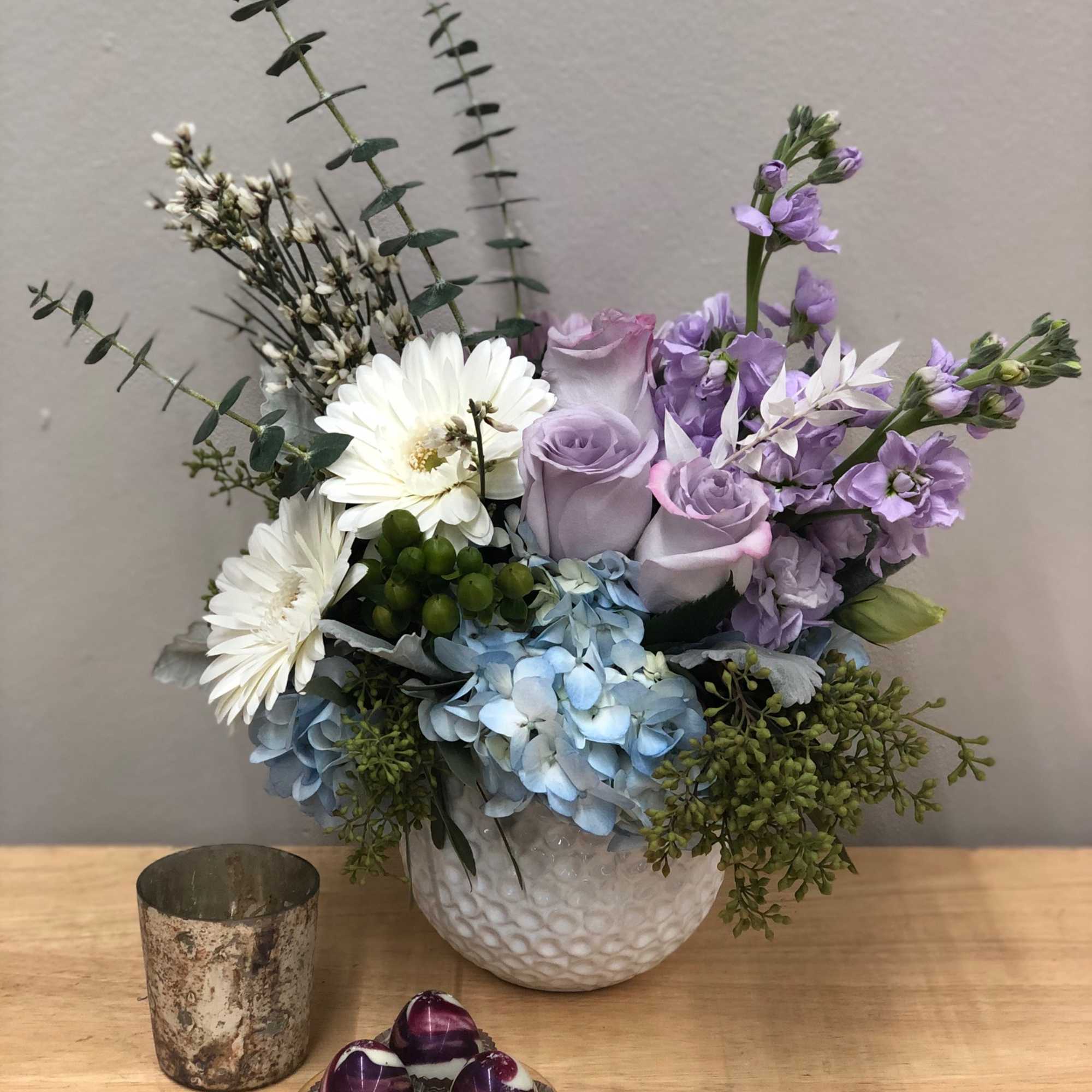 Lavender roses and white daisies in a white vase with blue hydrangeas