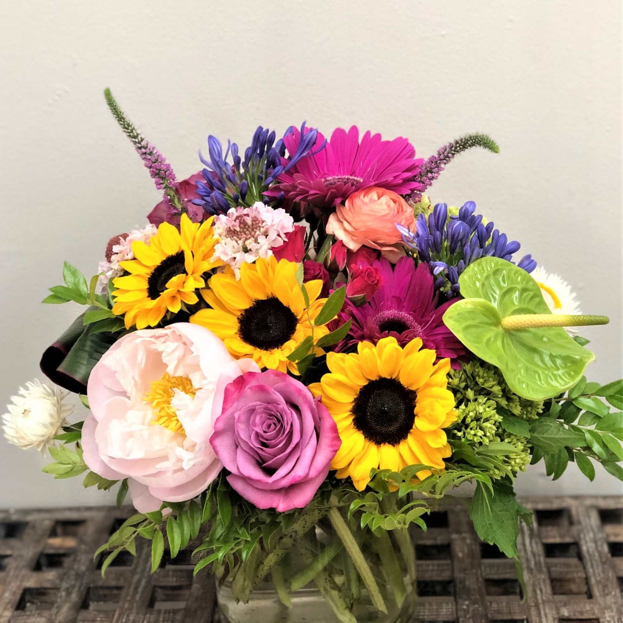 Colorful mixed flower arrangement with sunflowers, roses, and gerbera daisies in a glass vase.