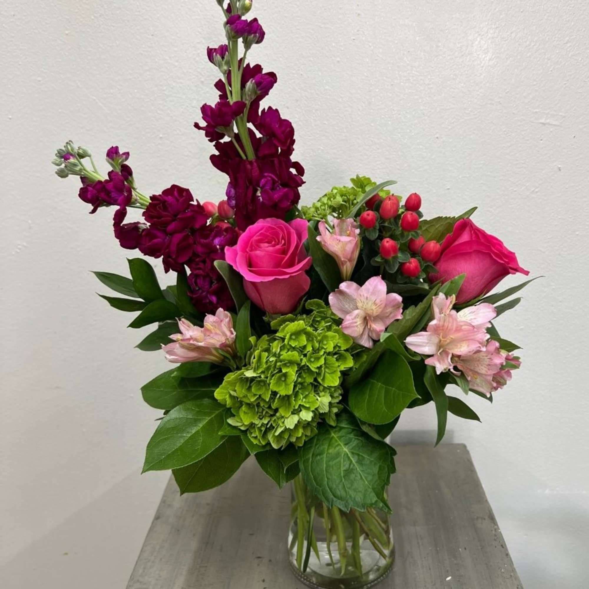 Bouquet of pink roses, green hydrangea, and purple blooms in a glass vase