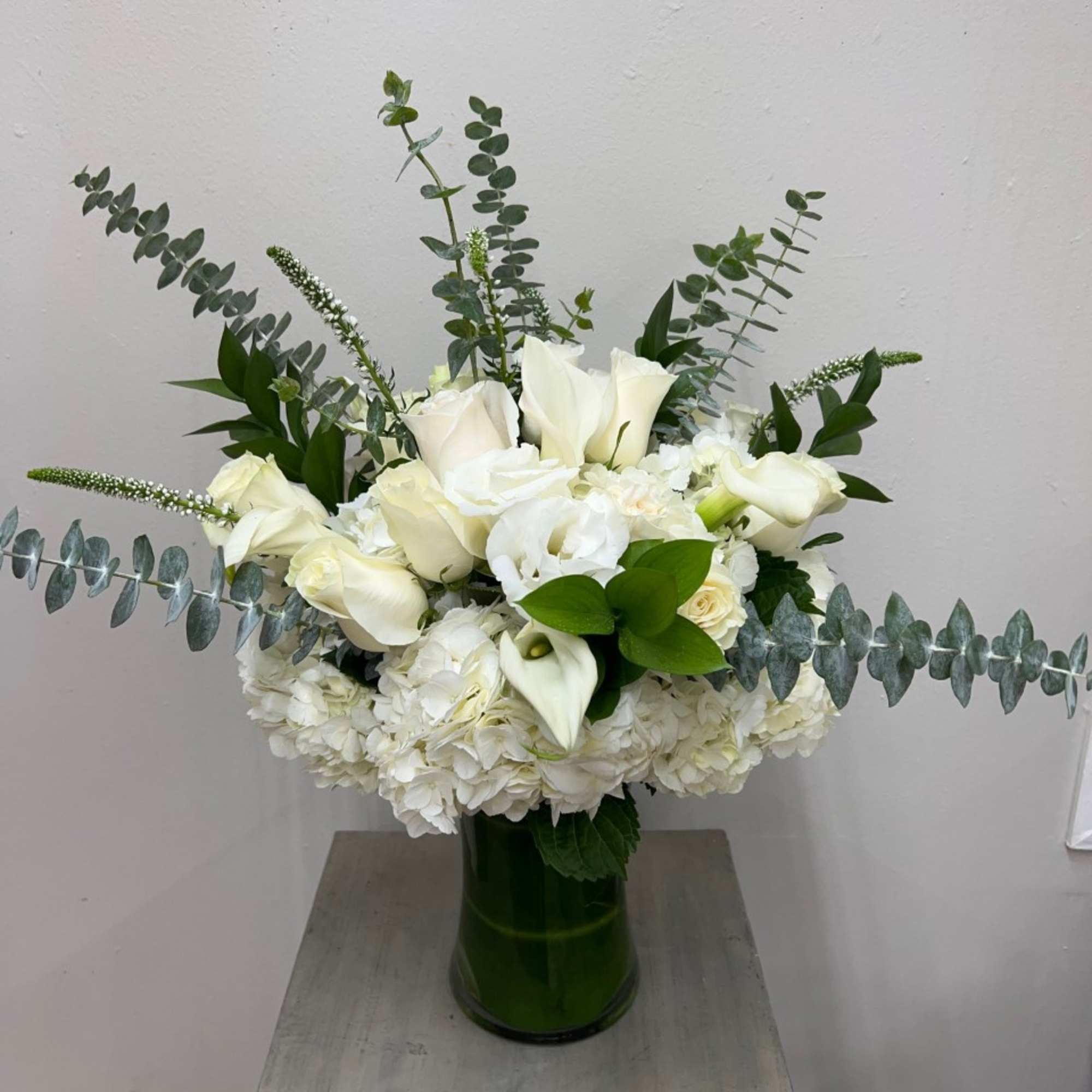 White floral arrangement in a green glass vase with eucalyptus accents
