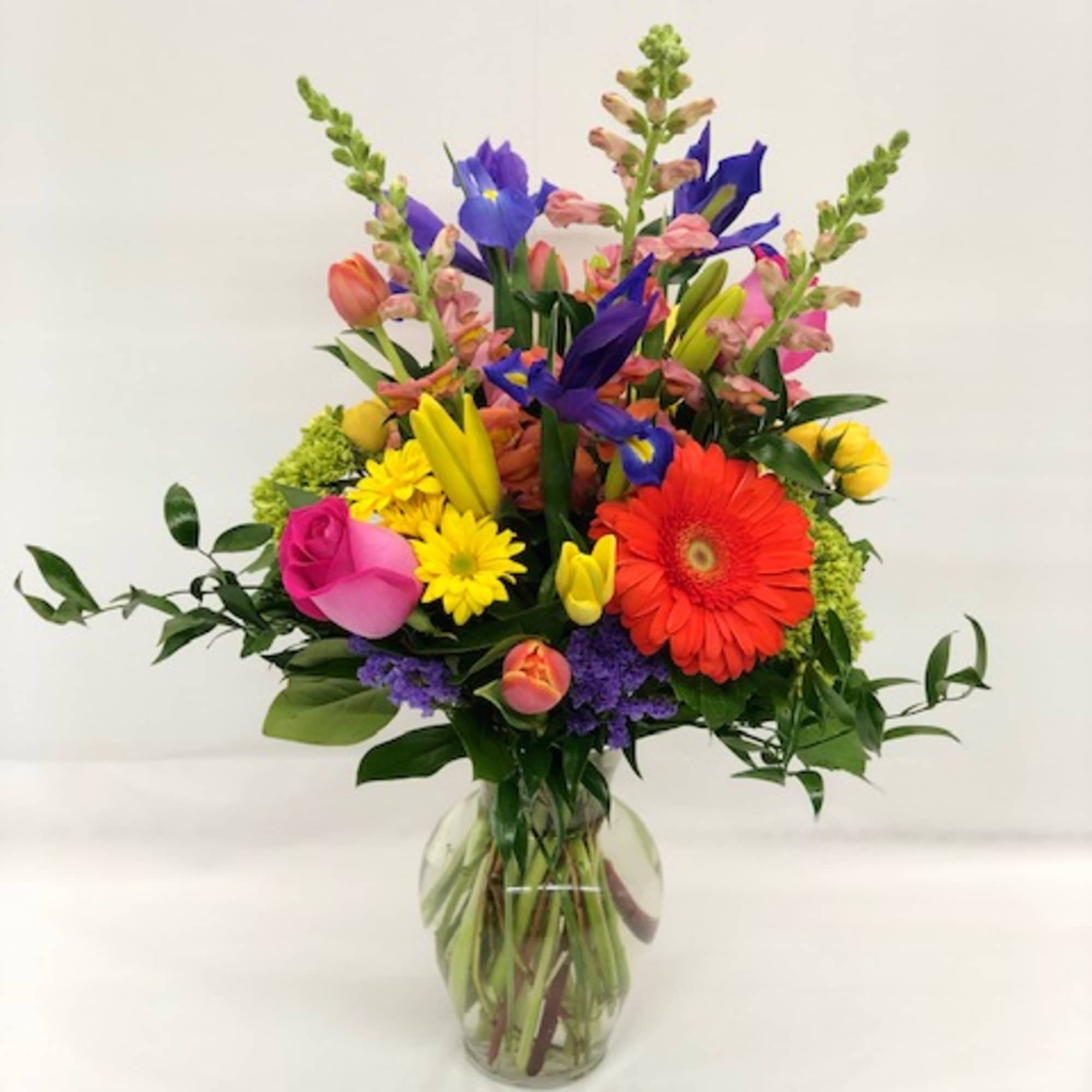 Tall mixed bouquet of bright roses, gerbera daisy, lilies, irises and tulips in a clear glass vase