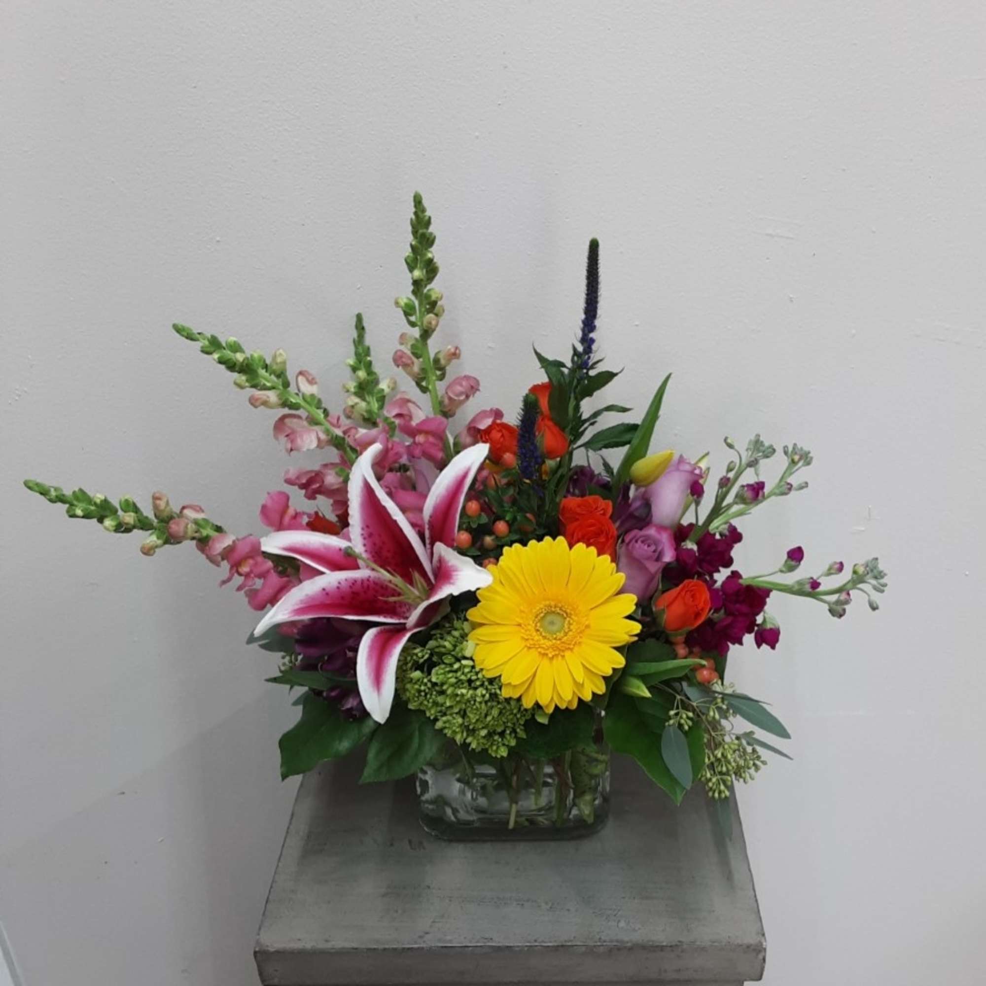 Low mixed arrangement with pink lilies, yellow gerbera daisy, roses and snapdragons in a clear glass vase