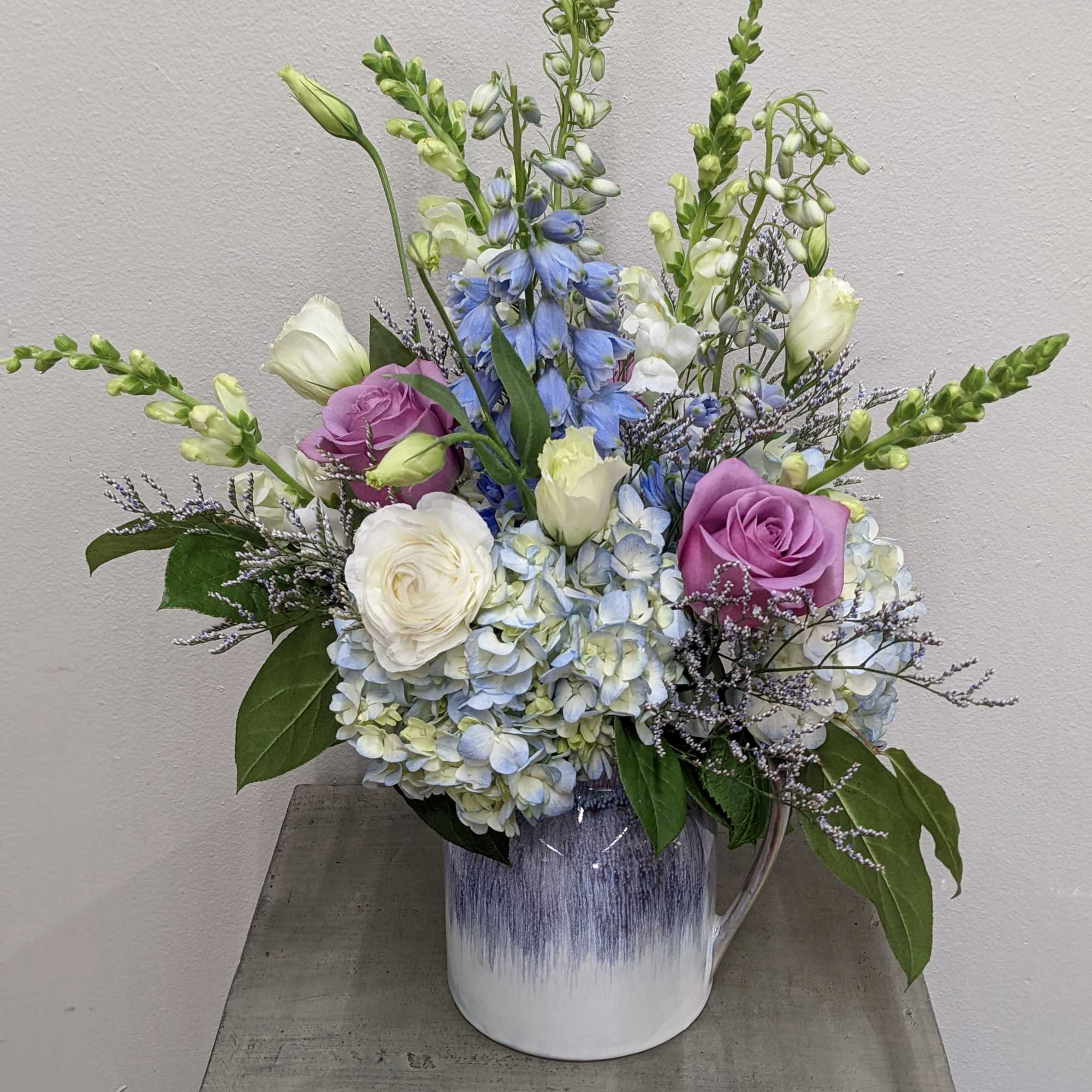 Mixed bouquet in a white ceramic vase with blue, white, and purple flowers