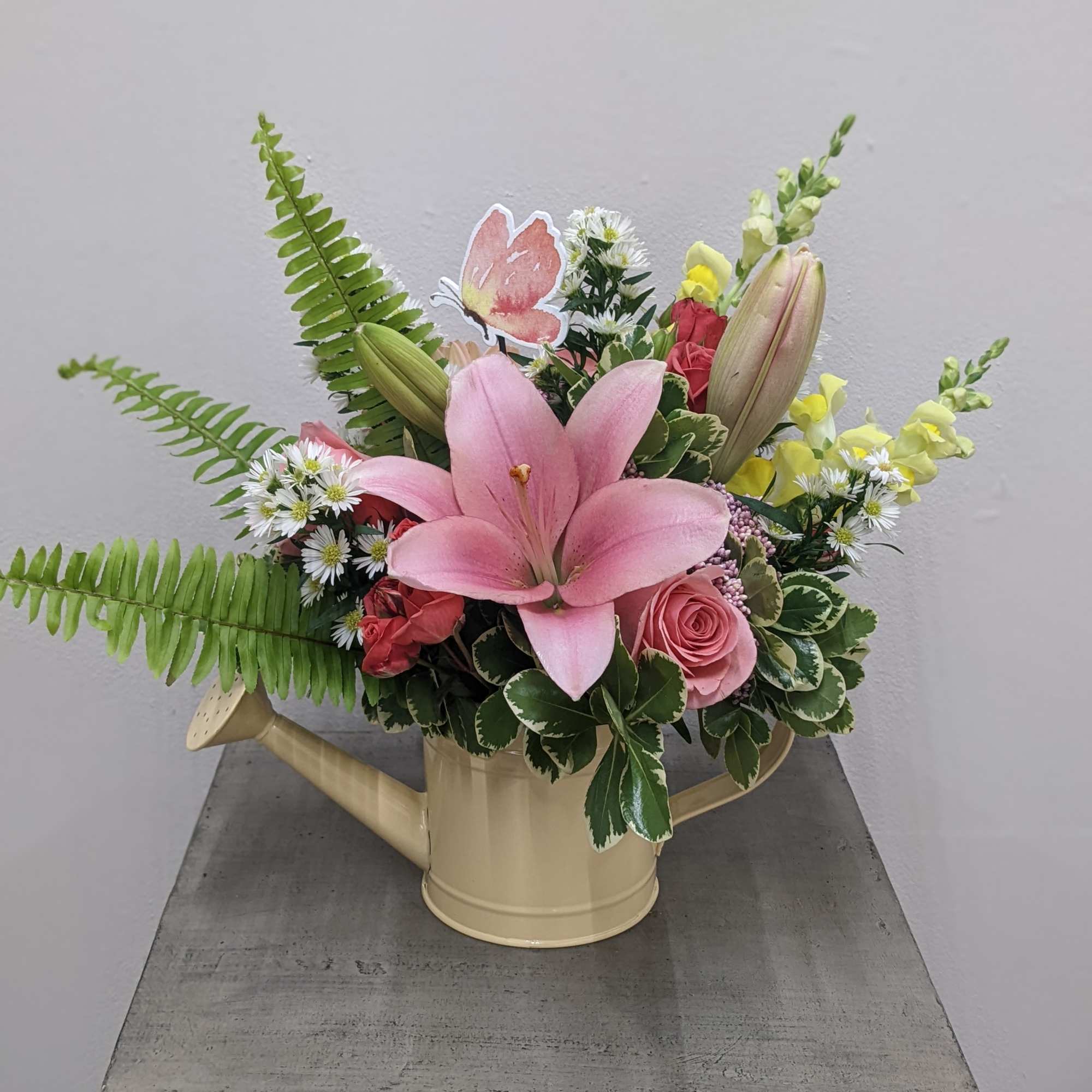 Pink lily and roses arranged in a watering can vase