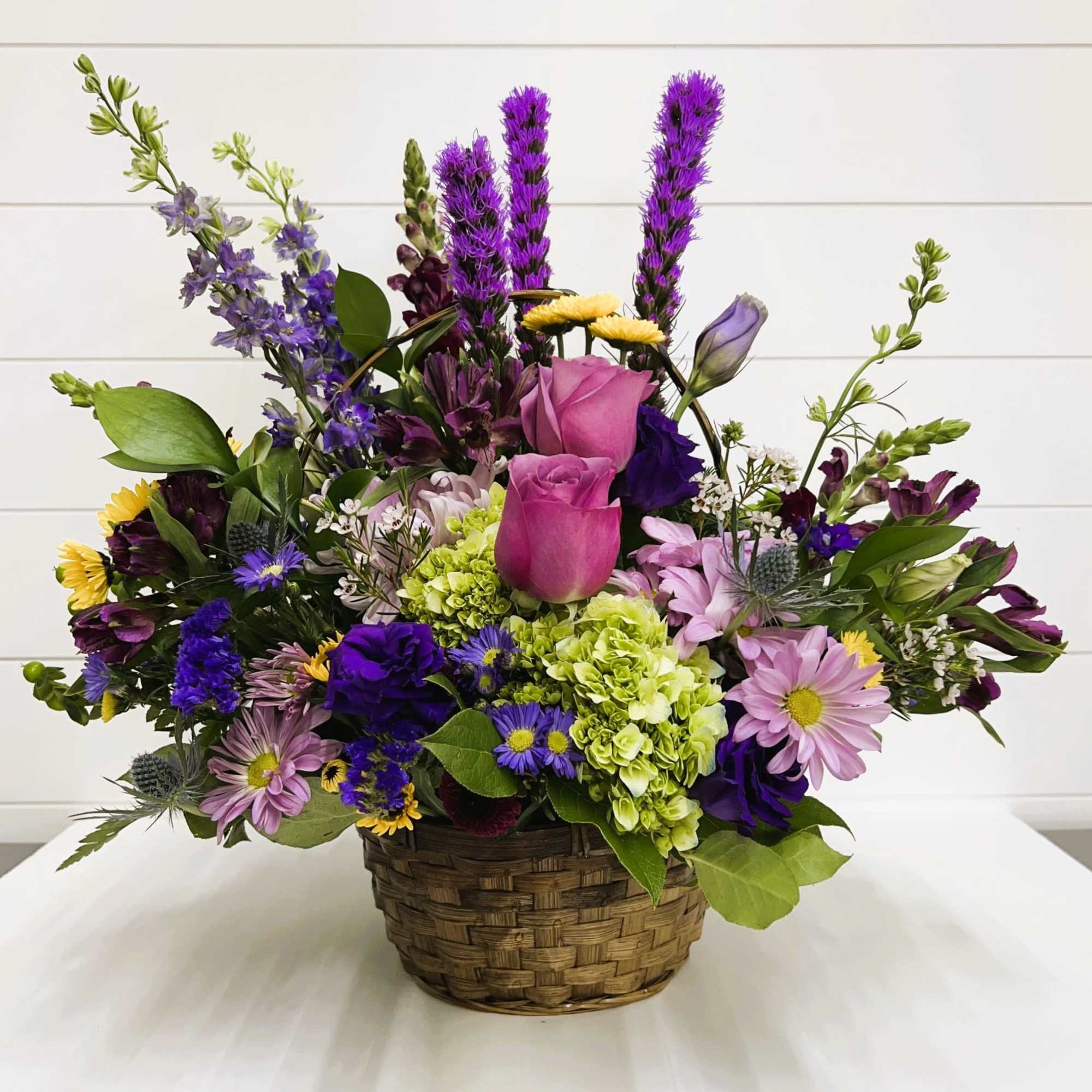 Mixed bouquet in a woven basket with pink, purple, yellow, and green flowers