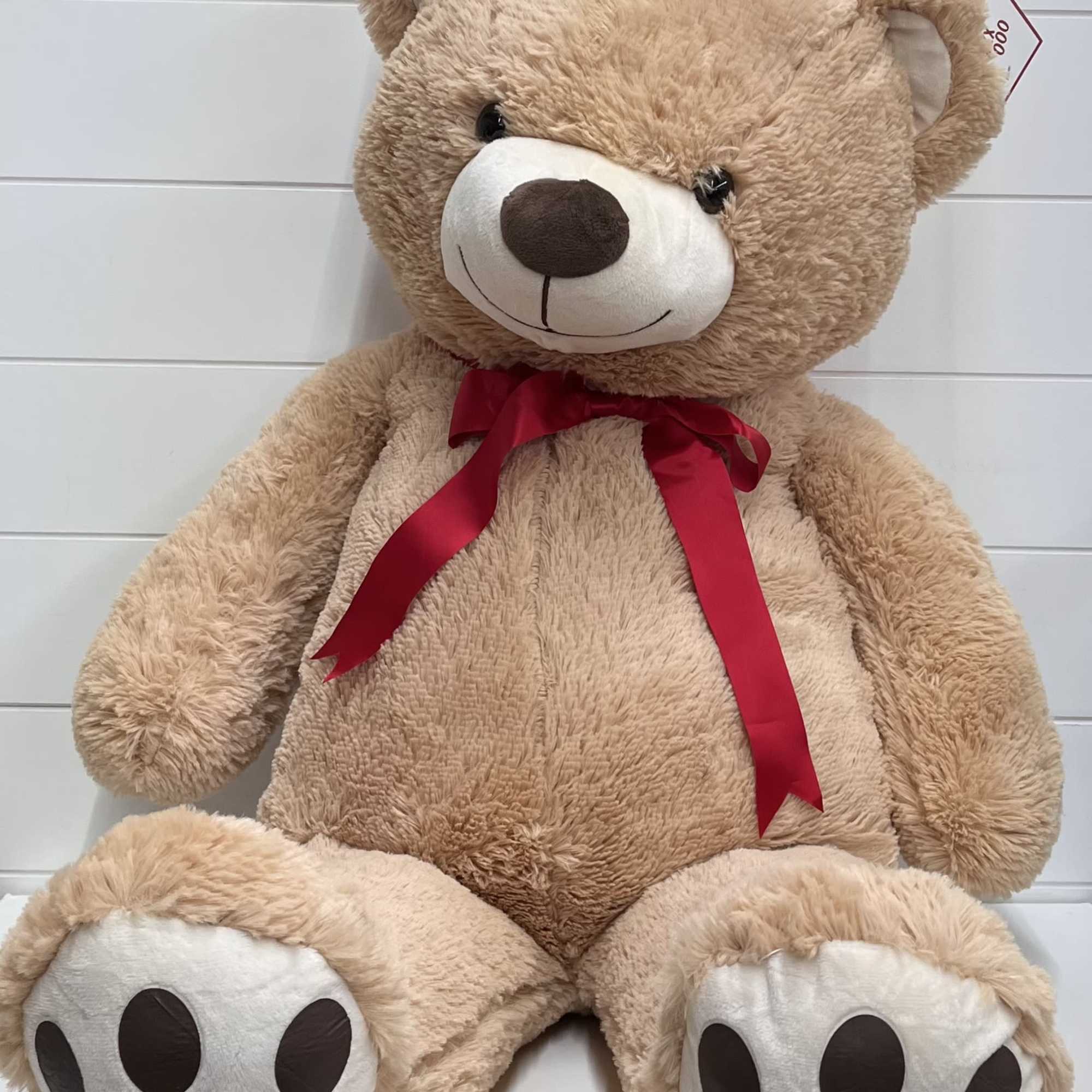 Large tan teddy bear with a red ribbon bow