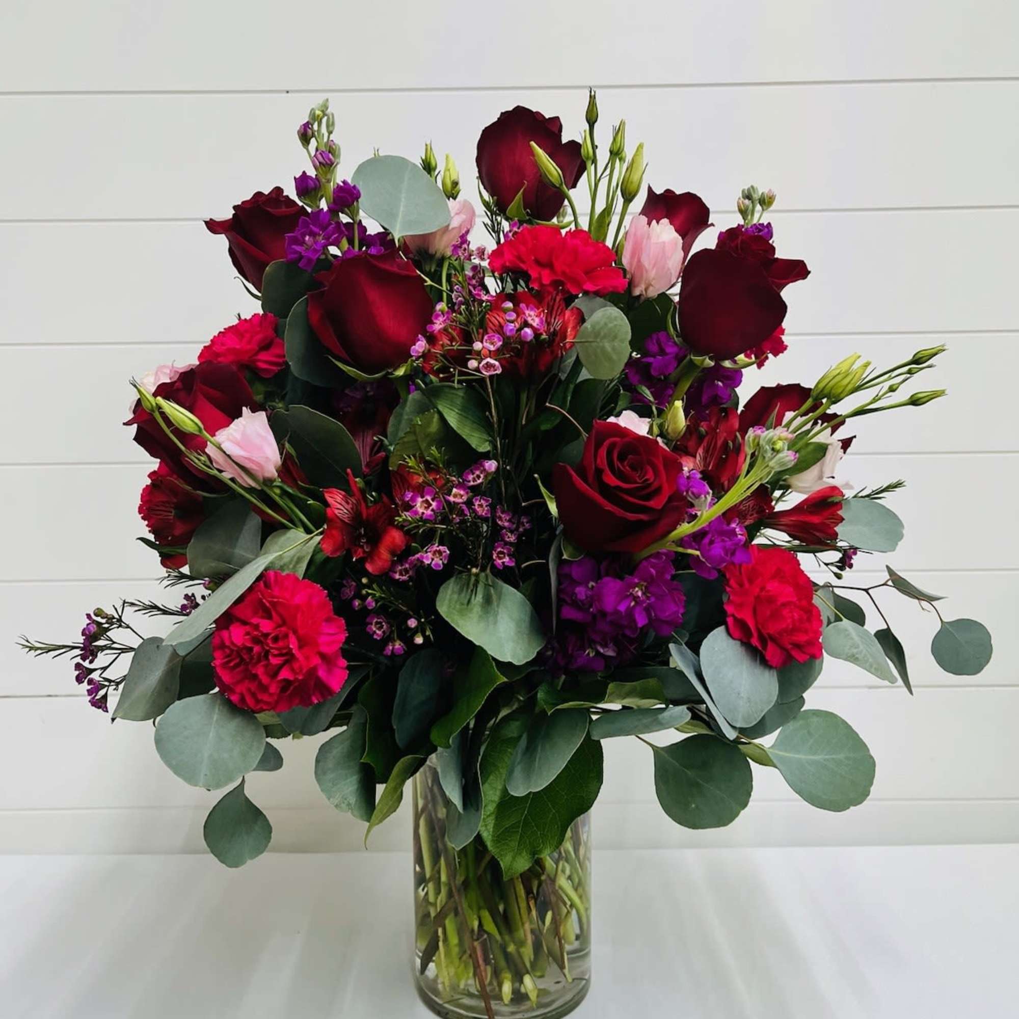 Bouquet of red roses, pink carnations, and purple flowers in a glass vase