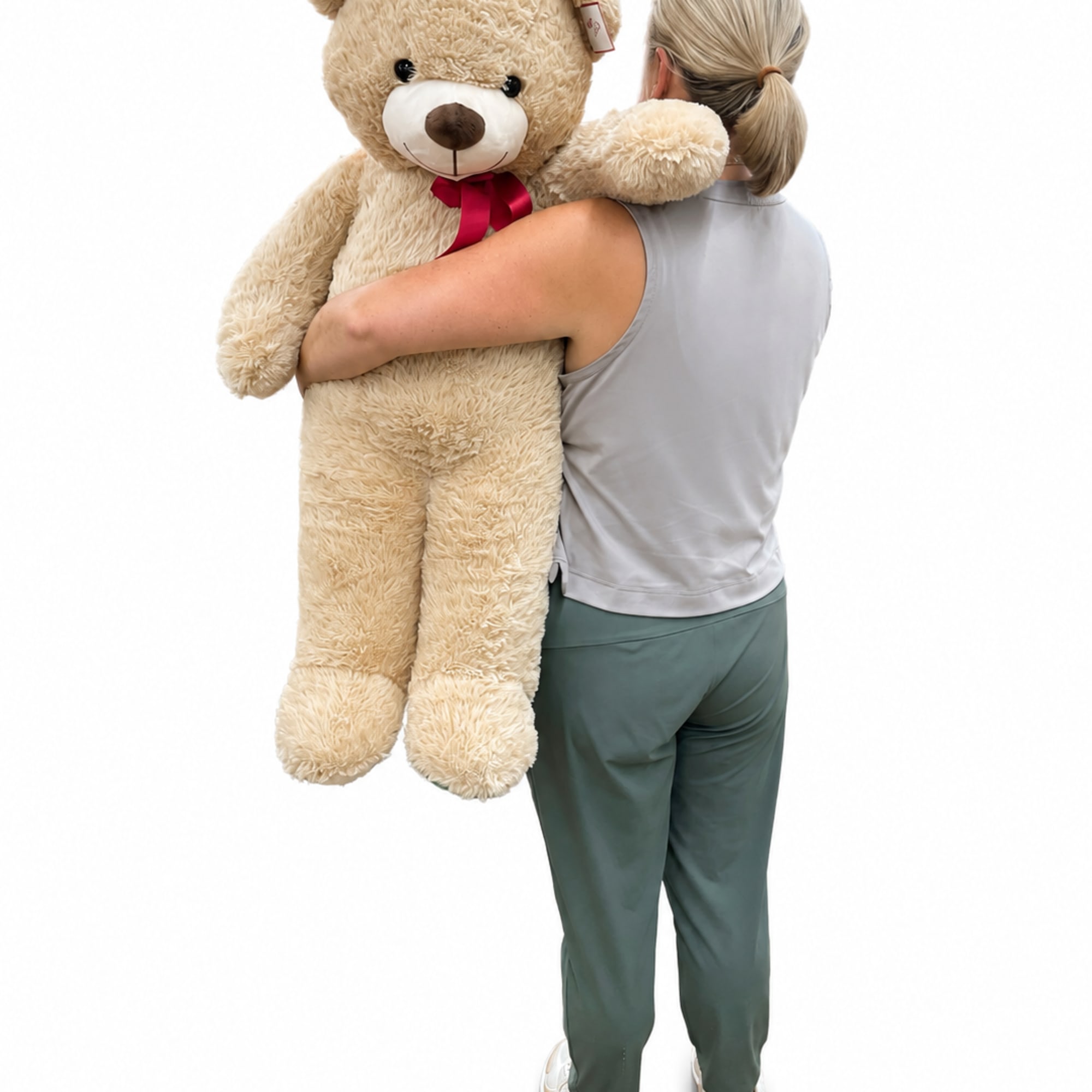 Person holding a large beige teddy bear with a red ribbon