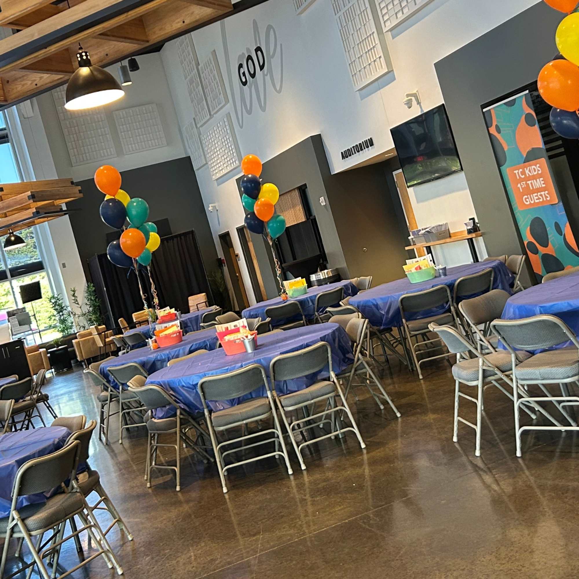 Decorated event room with balloon clusters and blue-covered tables