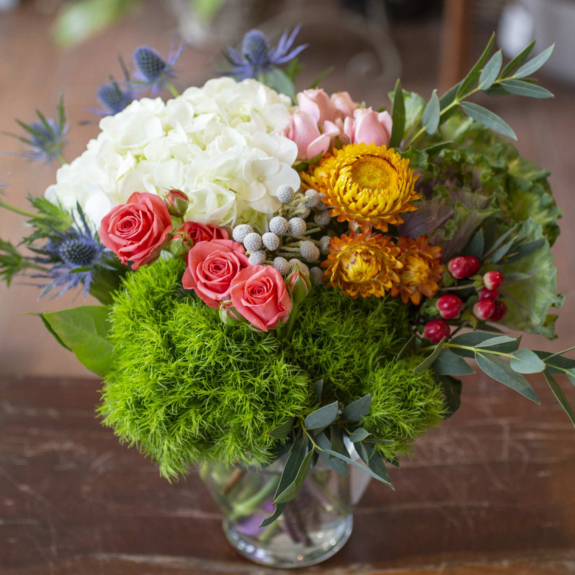 Mixed bouquet in a clear glass vase with white hydrangea, pink roses, and yellow blooms