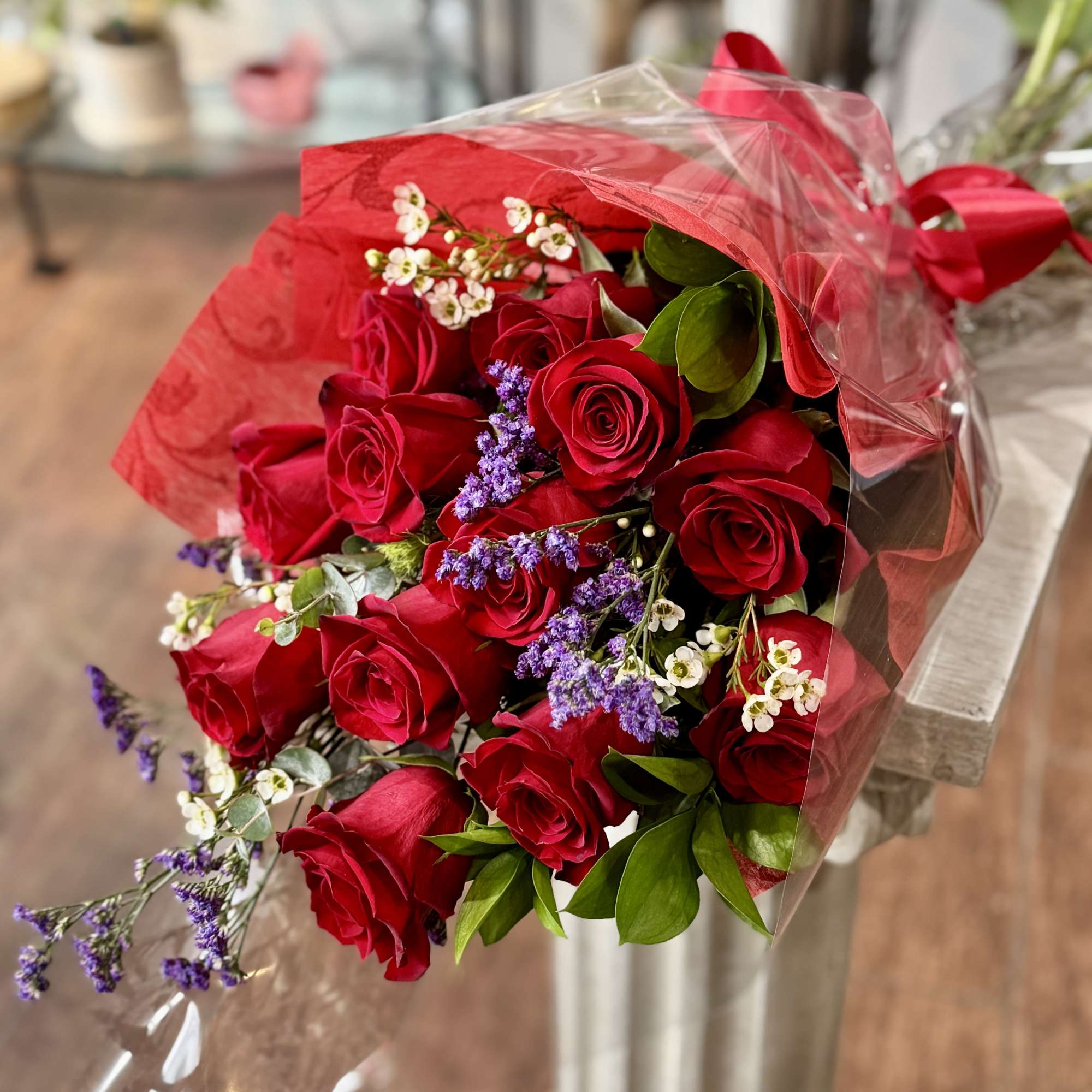 Bouquet of red roses with purple filler flowers wrapped in red and clear plastic