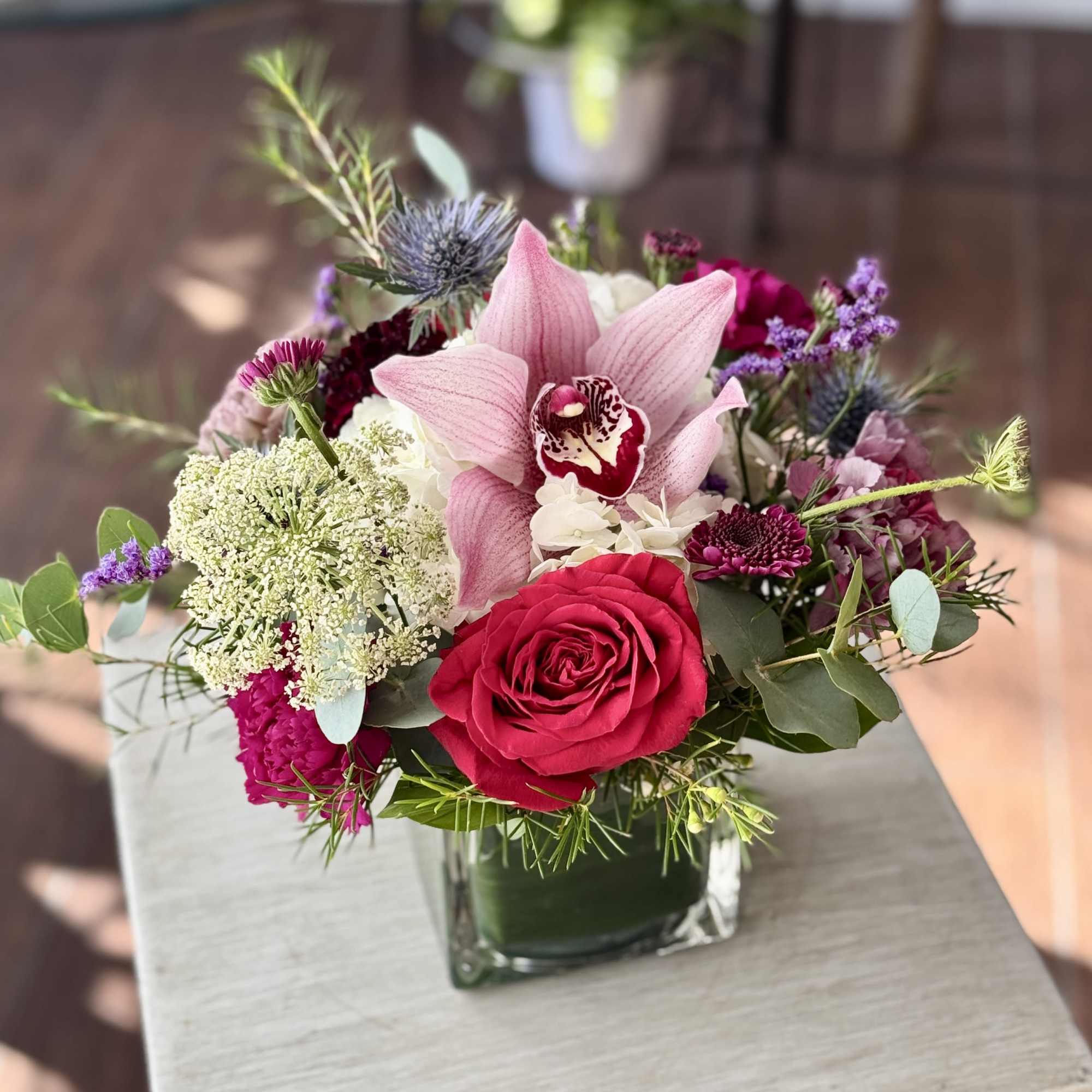 Pink orchid and red rose bouquet in a square glass vase