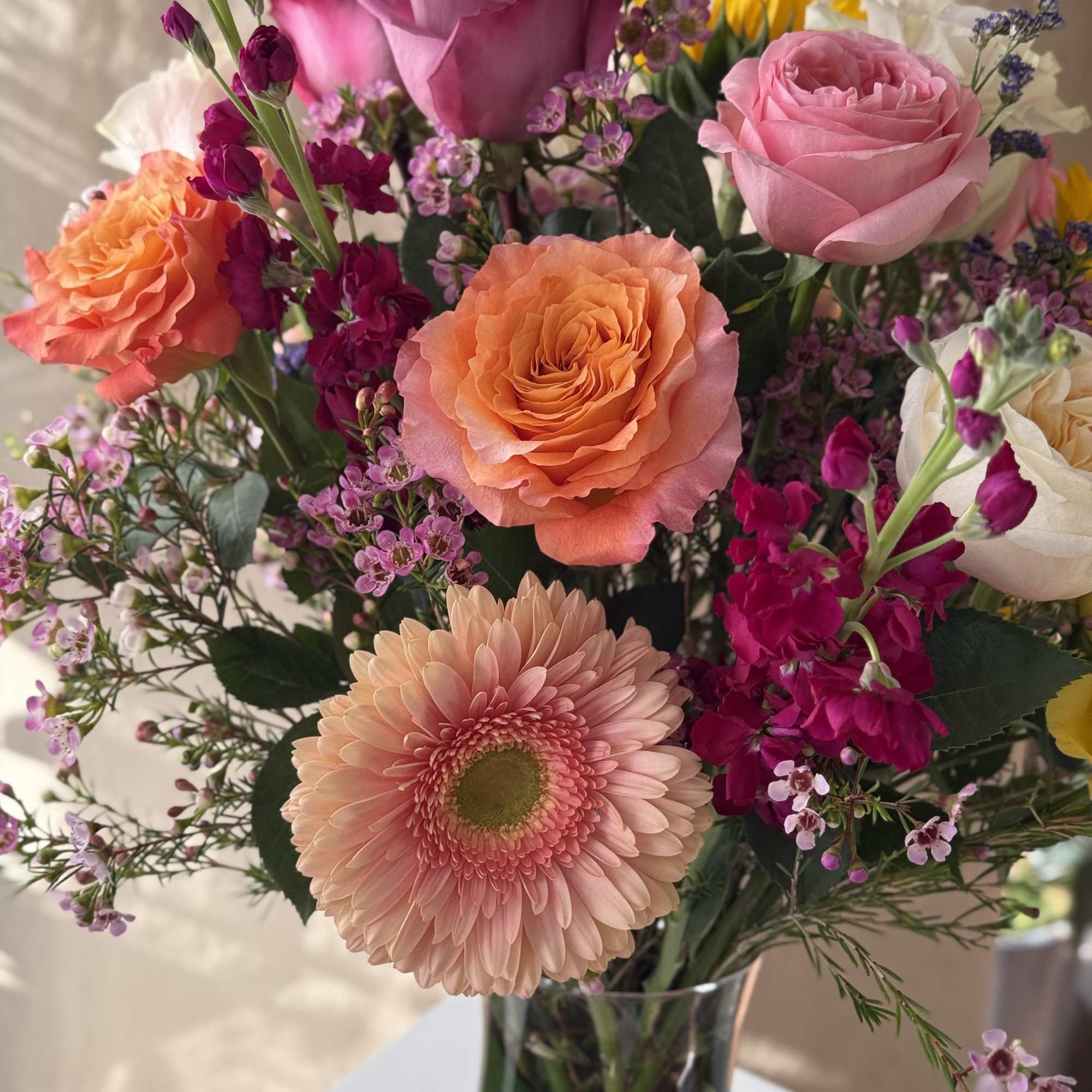 Mixed bouquet of pink, peach, and purple flowers in a glass vase