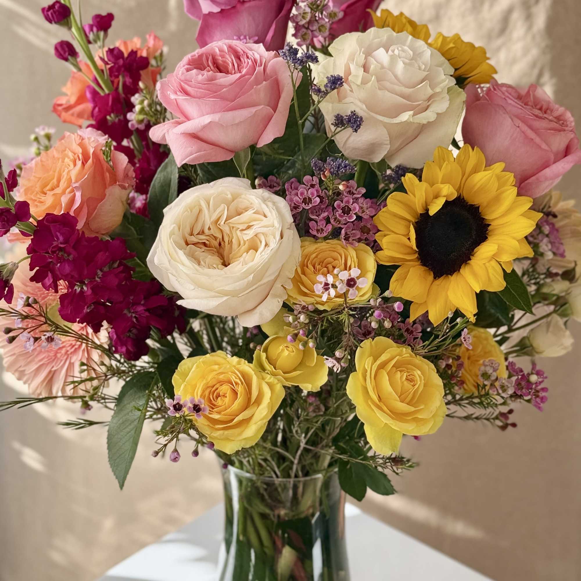 Mixed bouquet of roses, sunflowers, and small purple flowers in a glass vase