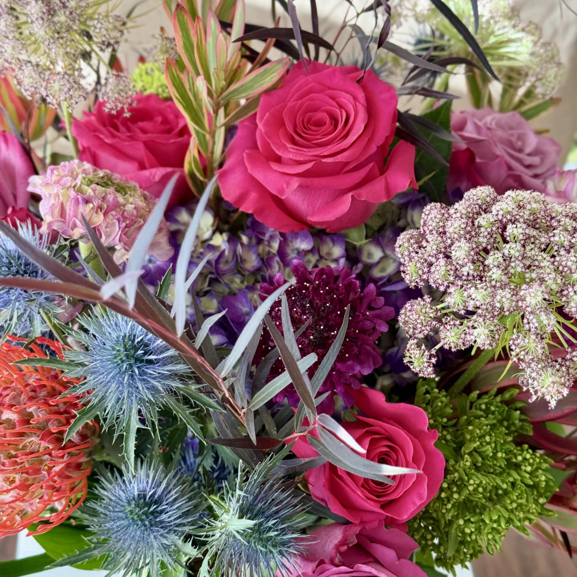 Bouquet of hot pink roses with spiky blue thistles and mixed blooms