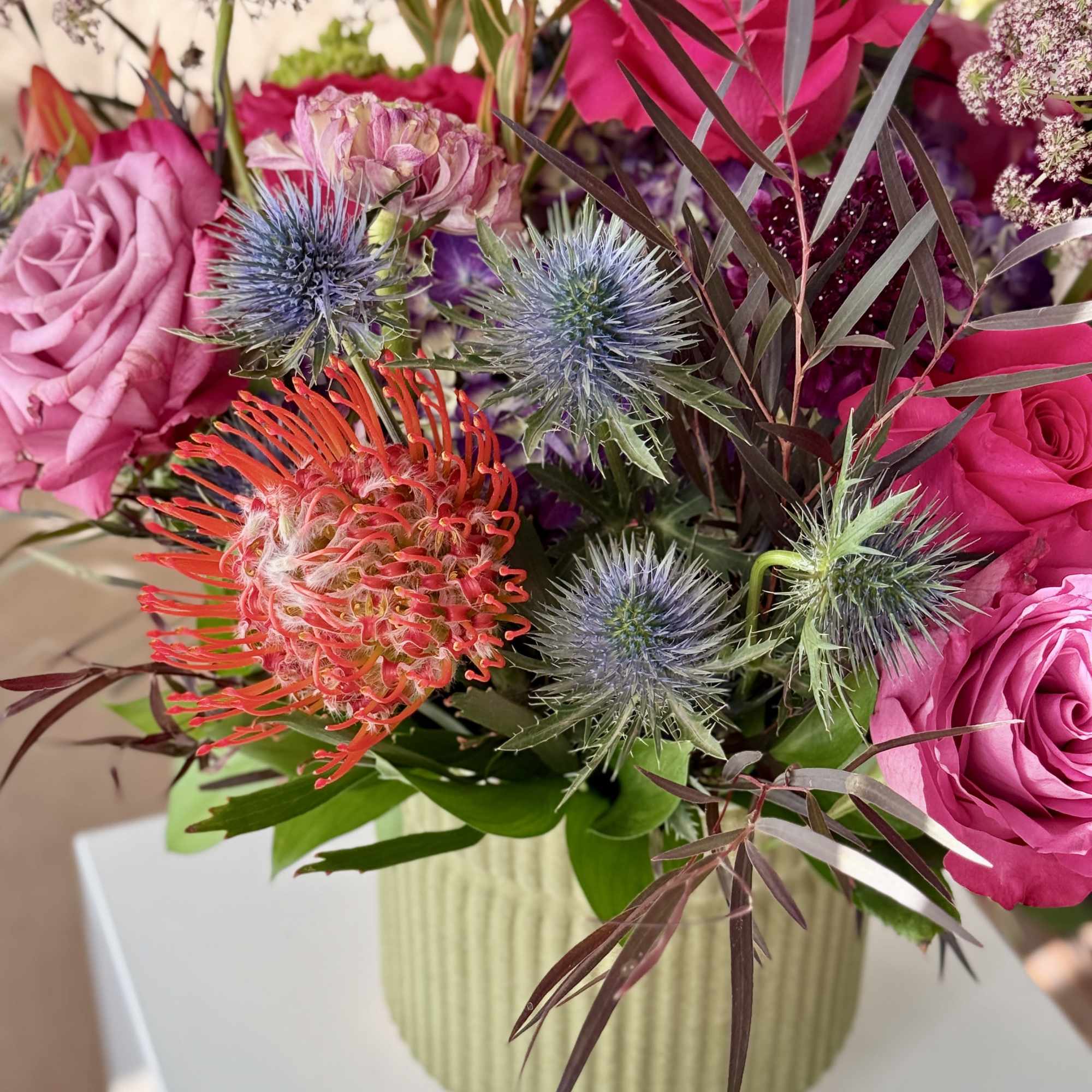Pink roses and spiky thistle flowers in a ribbed vase