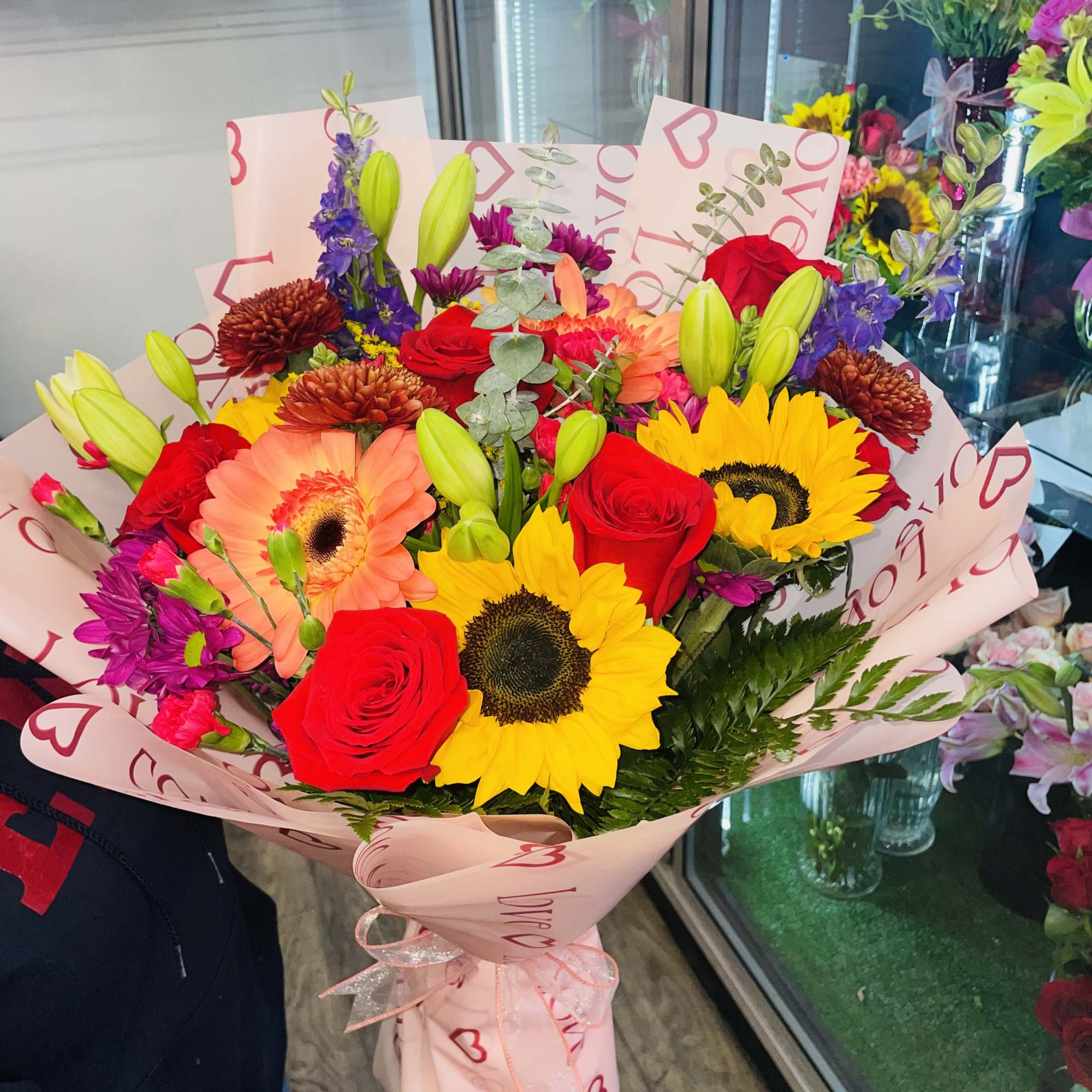 Mixed bouquet with roses, sunflowers, and gerbera daisies in pink wrap