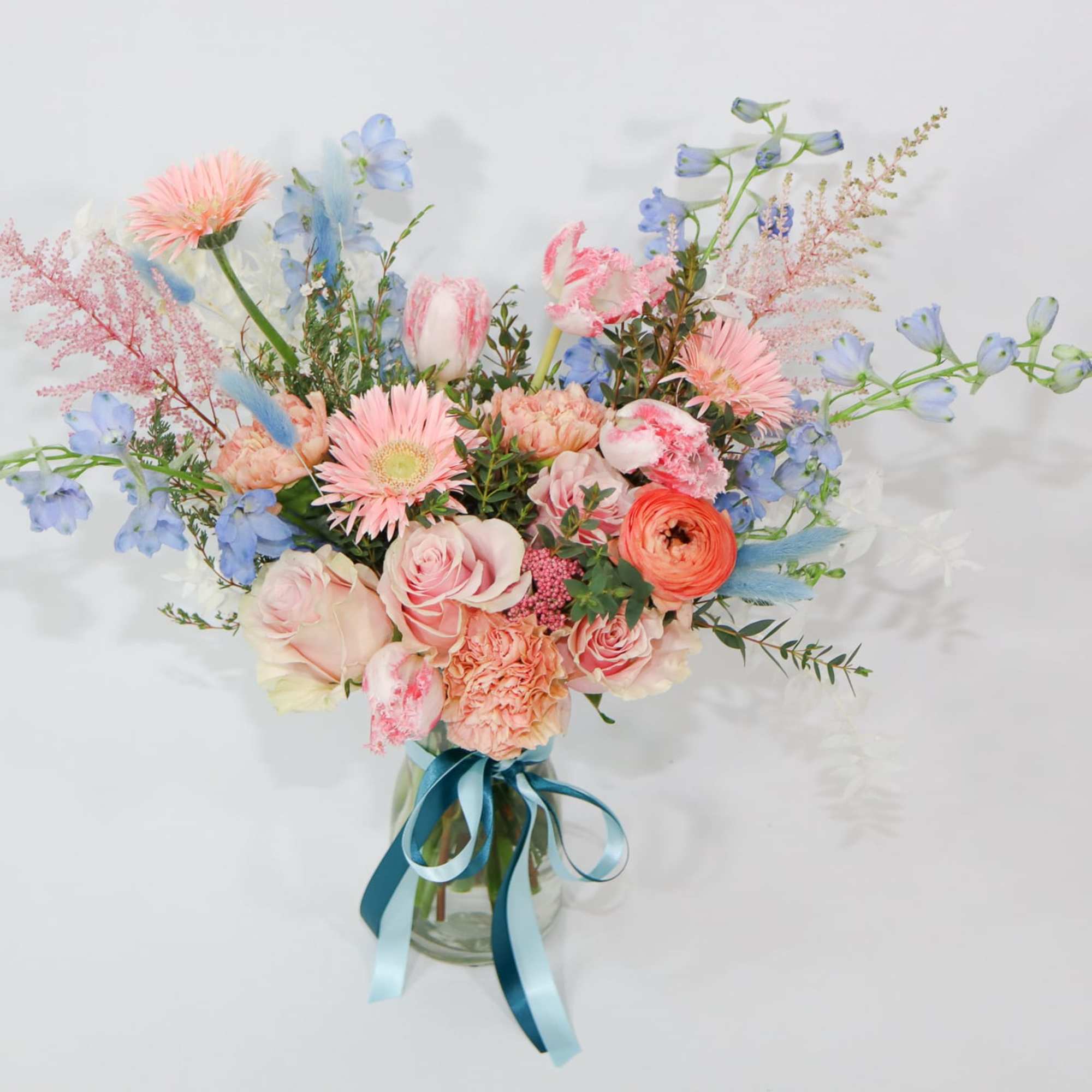Pastel mixed flower bouquet in a glass vase with blue ribbon
