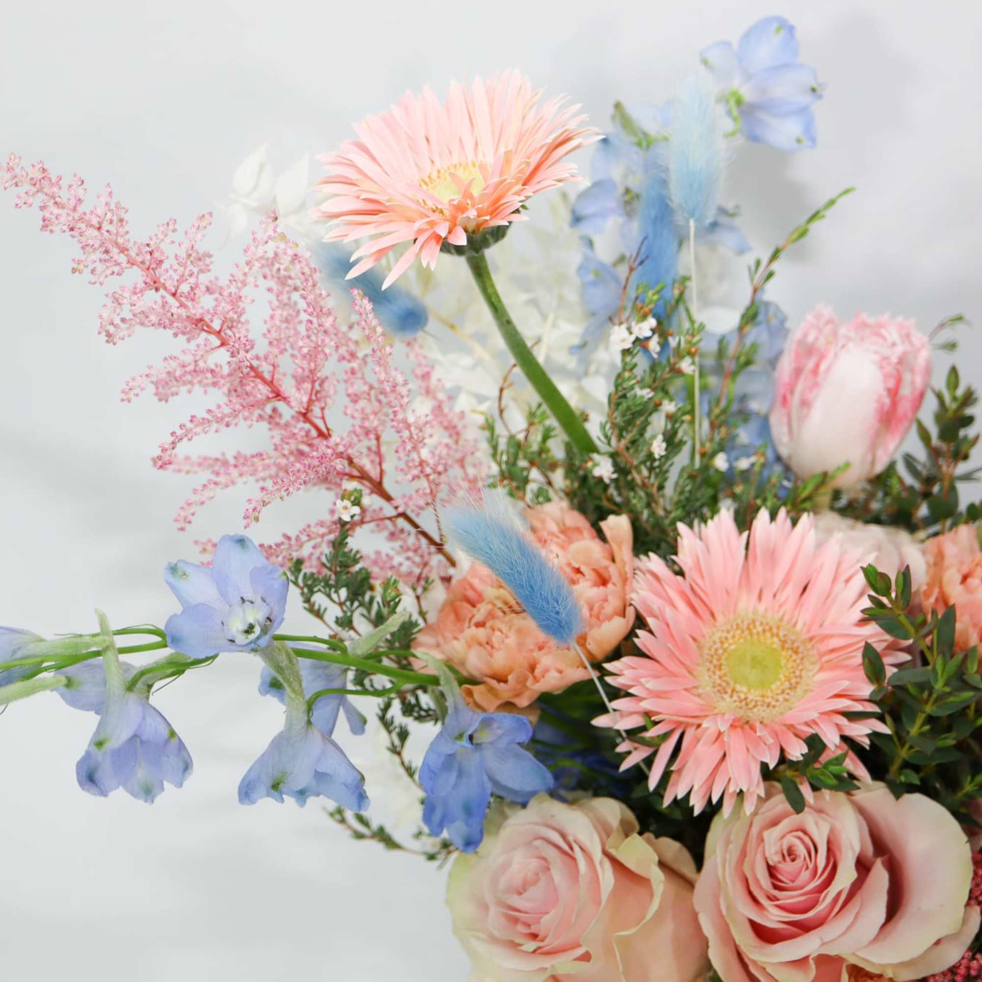 Pastel bouquet with pink gerbera daisies, roses, and blue flowers