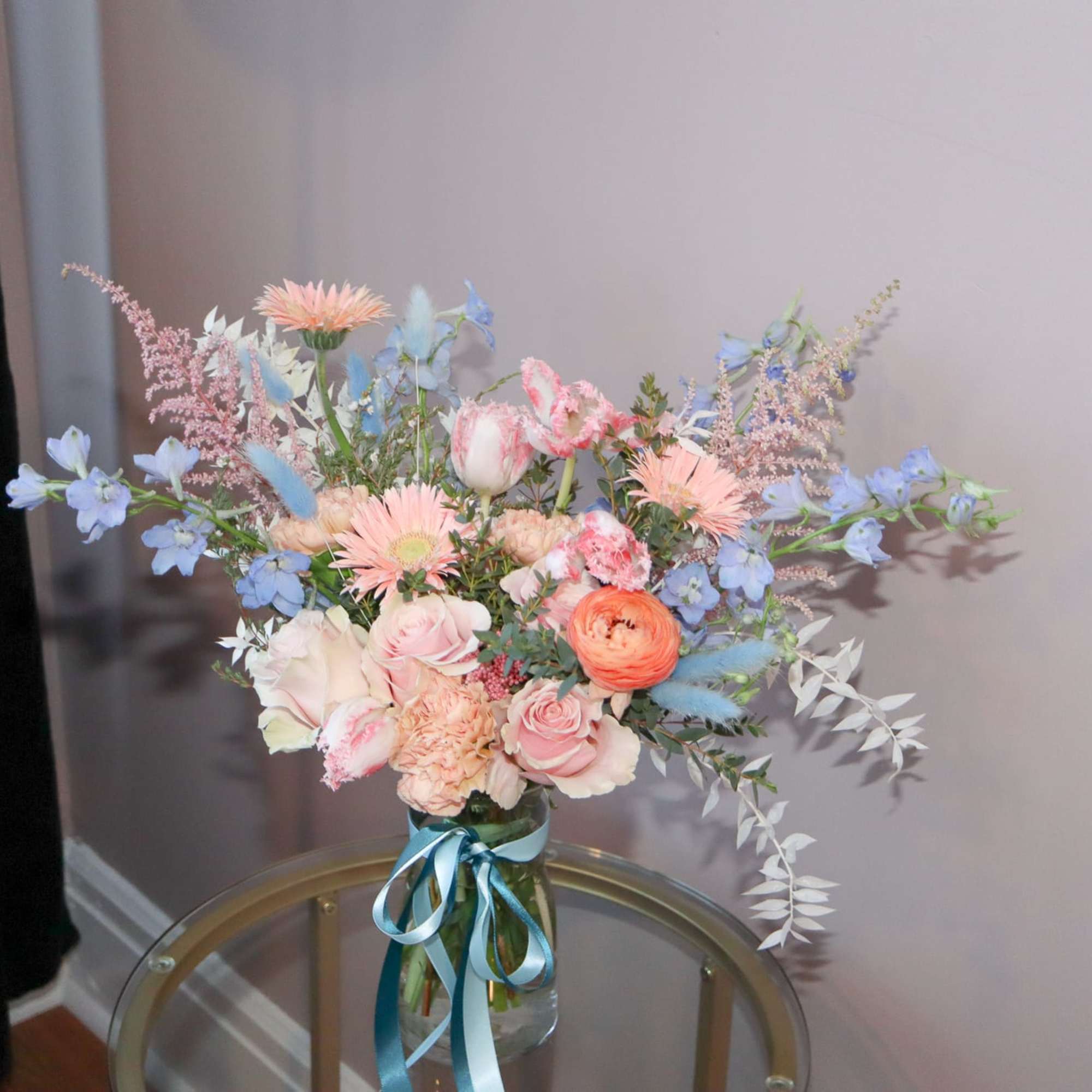 Pastel bouquet of mixed flowers in a glass vase with blue ribbon