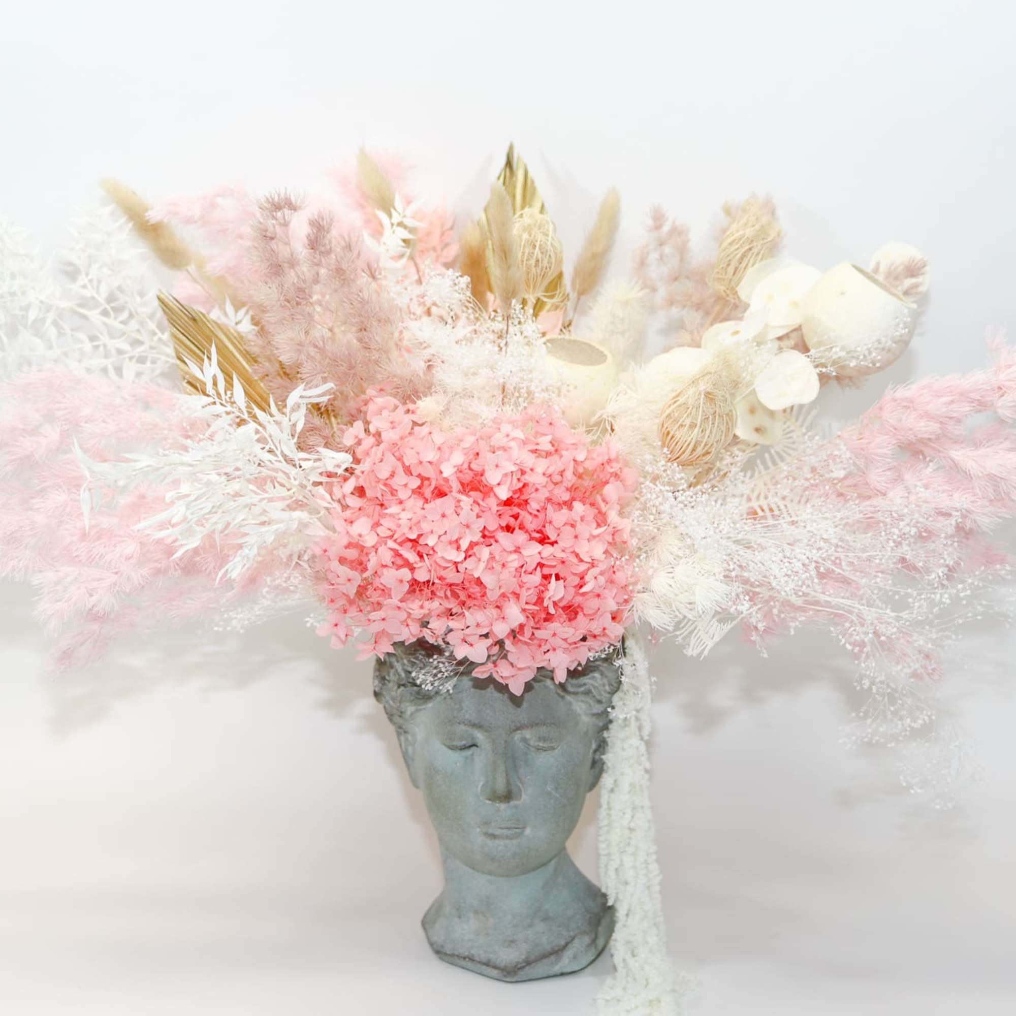 Pink and white dried floral arrangement in a gray bust vase