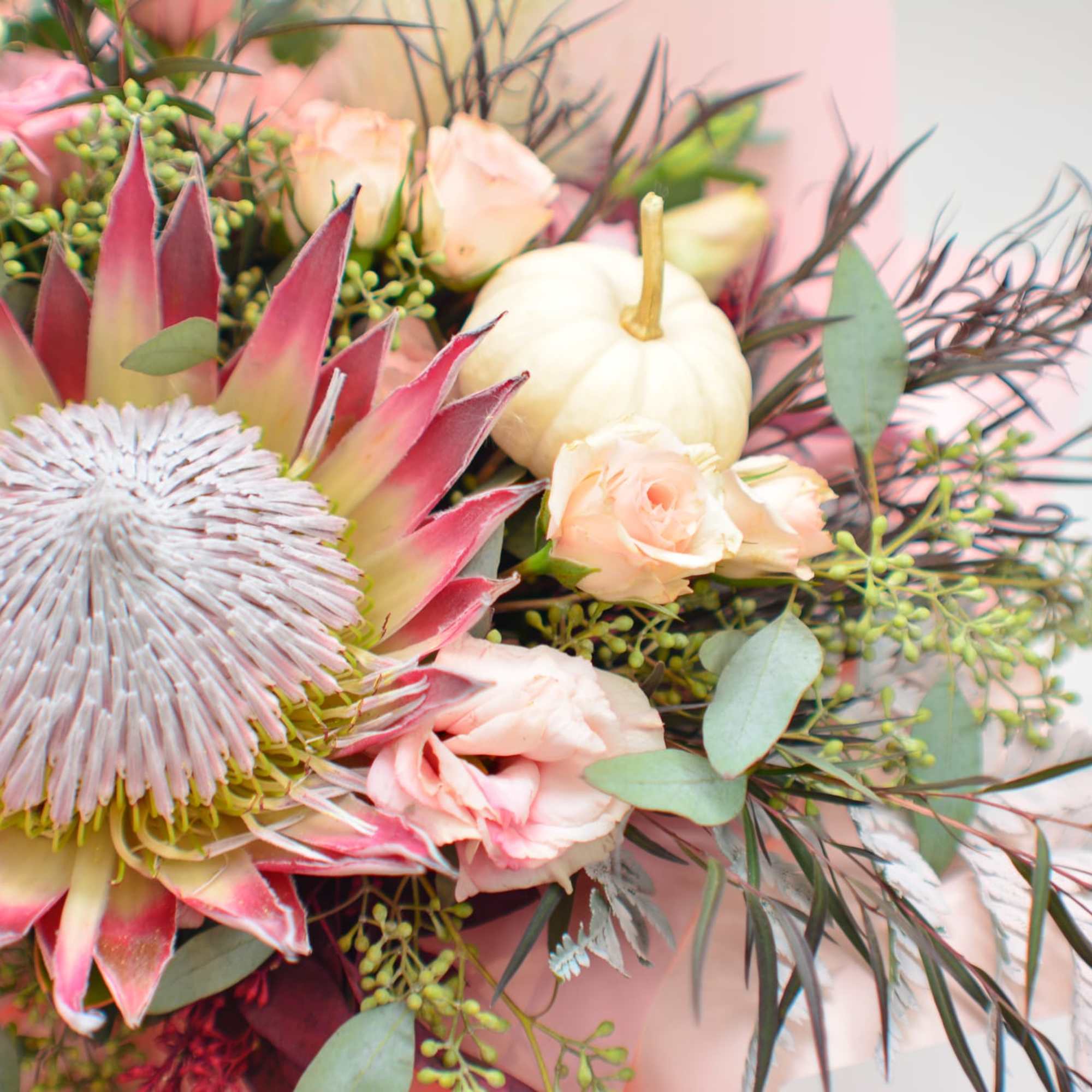 Bouquet with a large pink protea and pale roses, plus a small white pumpkin accent