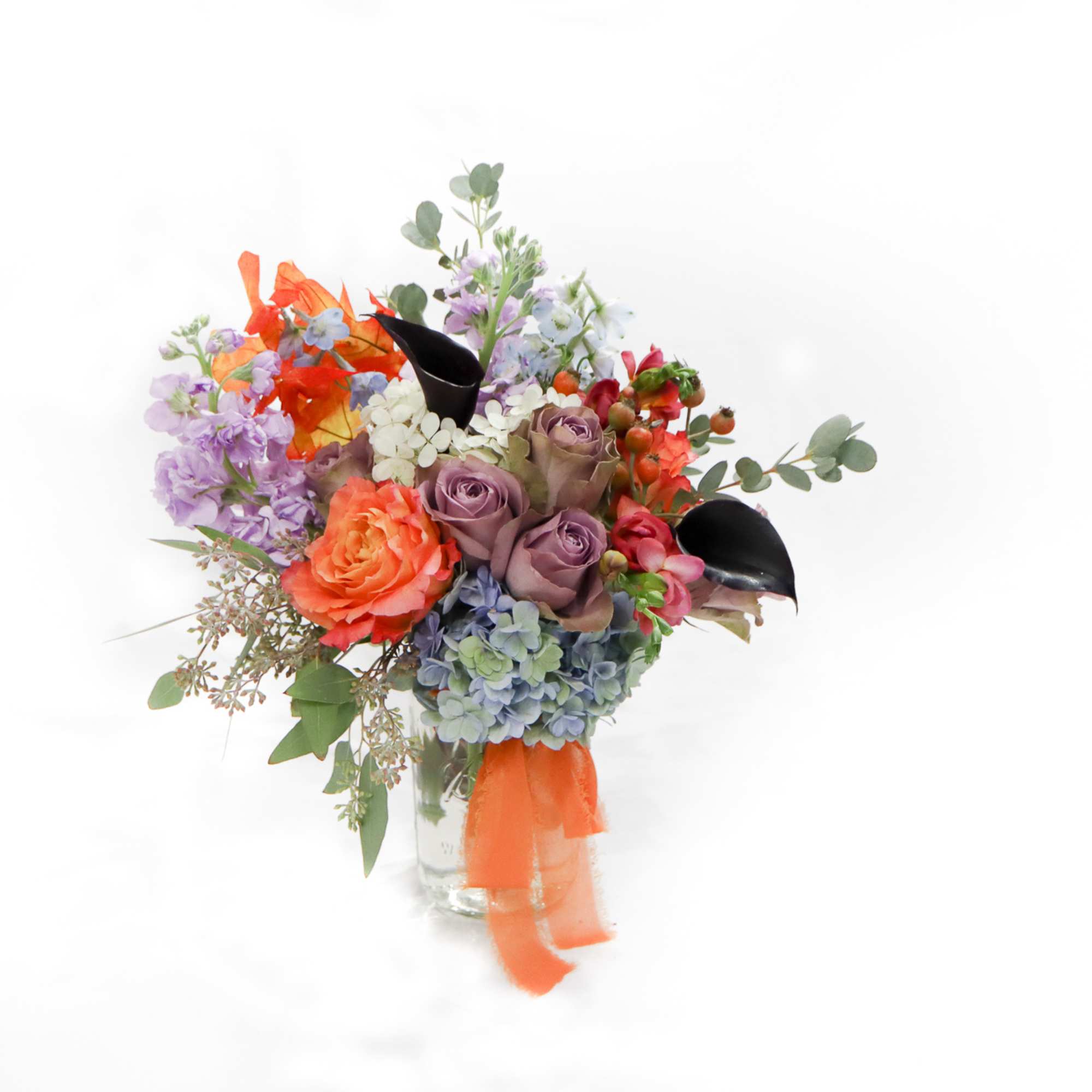 Mixed bouquet of roses, hydrangeas, and calla lilies in a clear vase