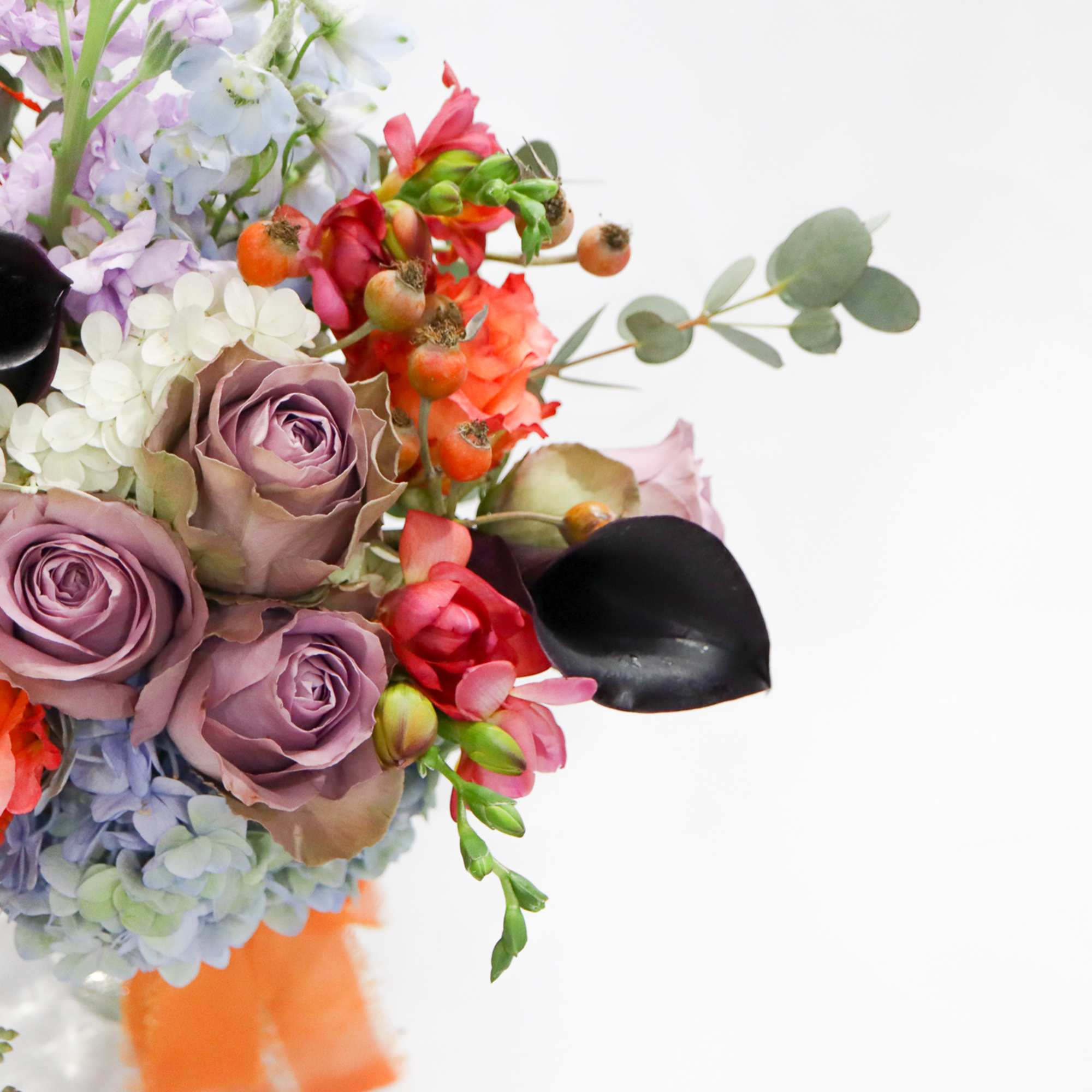 Bouquet of lavender roses, orange blooms, and black calla lilies