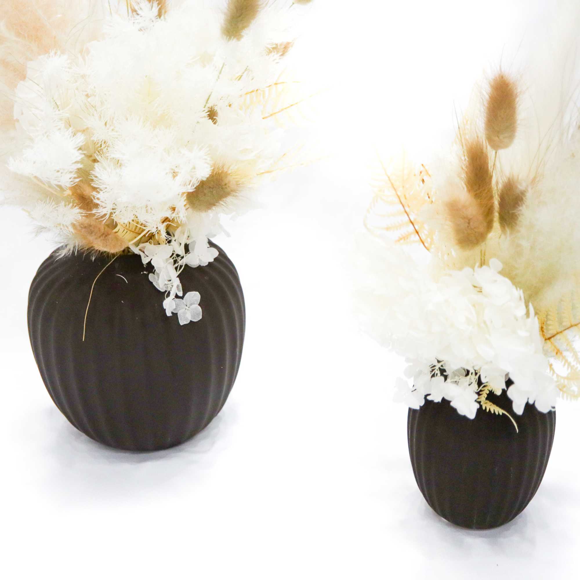 Two dried floral arrangements in dark vases with white and tan plumes