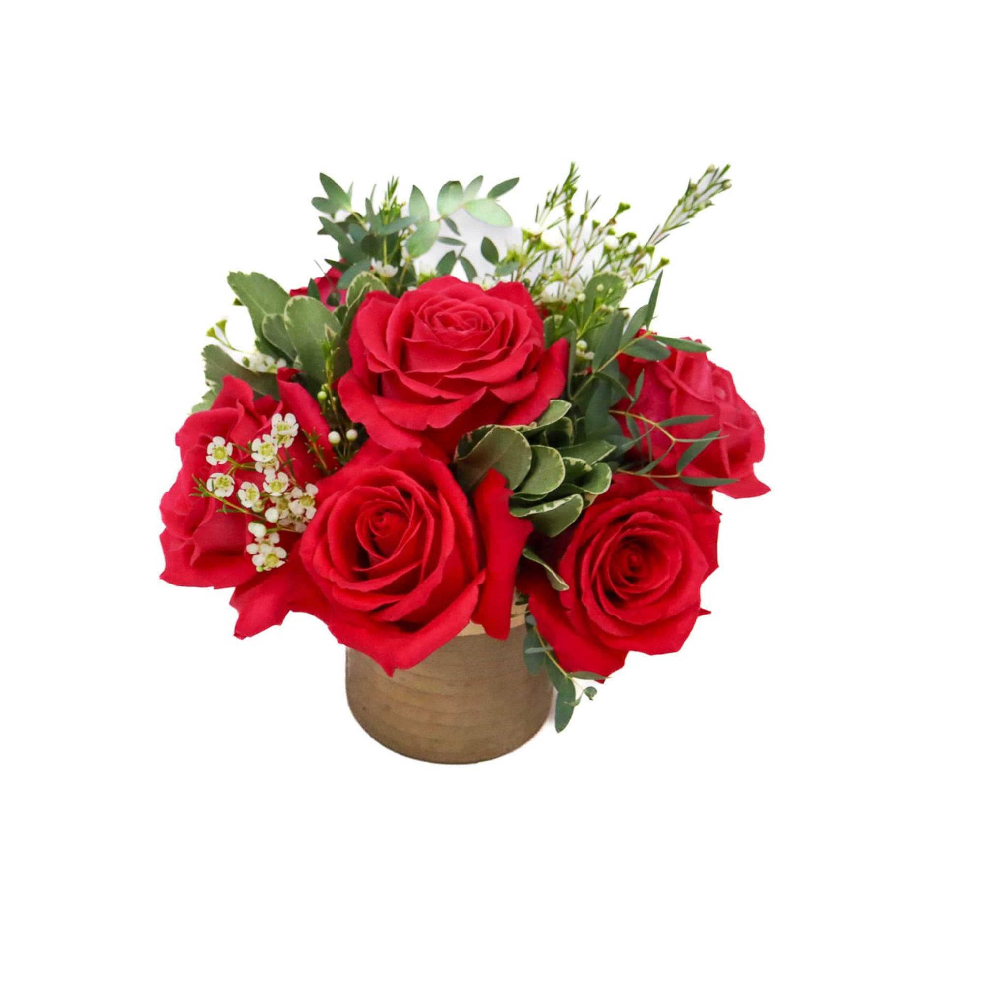 Red roses arranged in a small tan vase with greenery