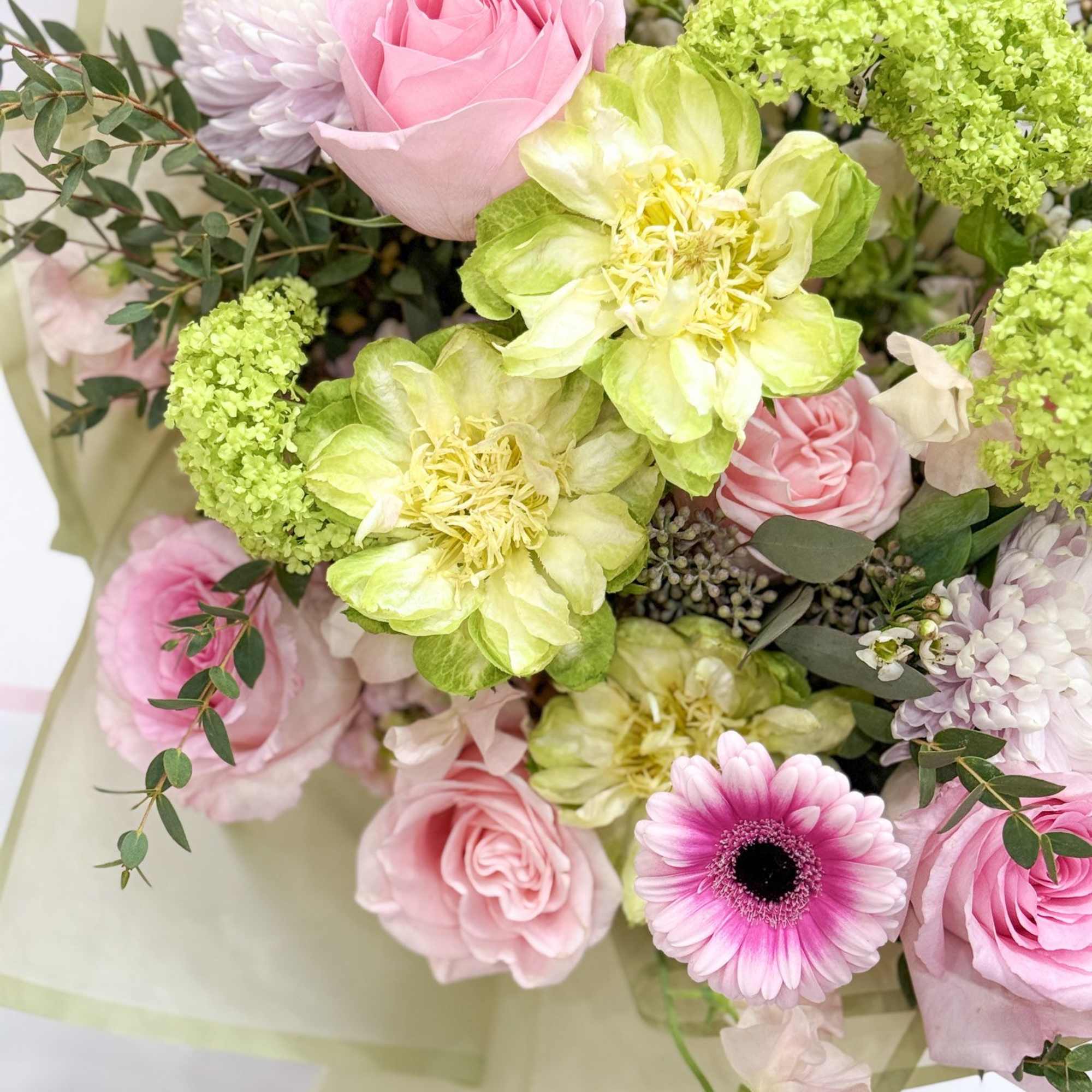 Pink roses and green blooms in a wrapped bouquet with a pink gerbera daisy