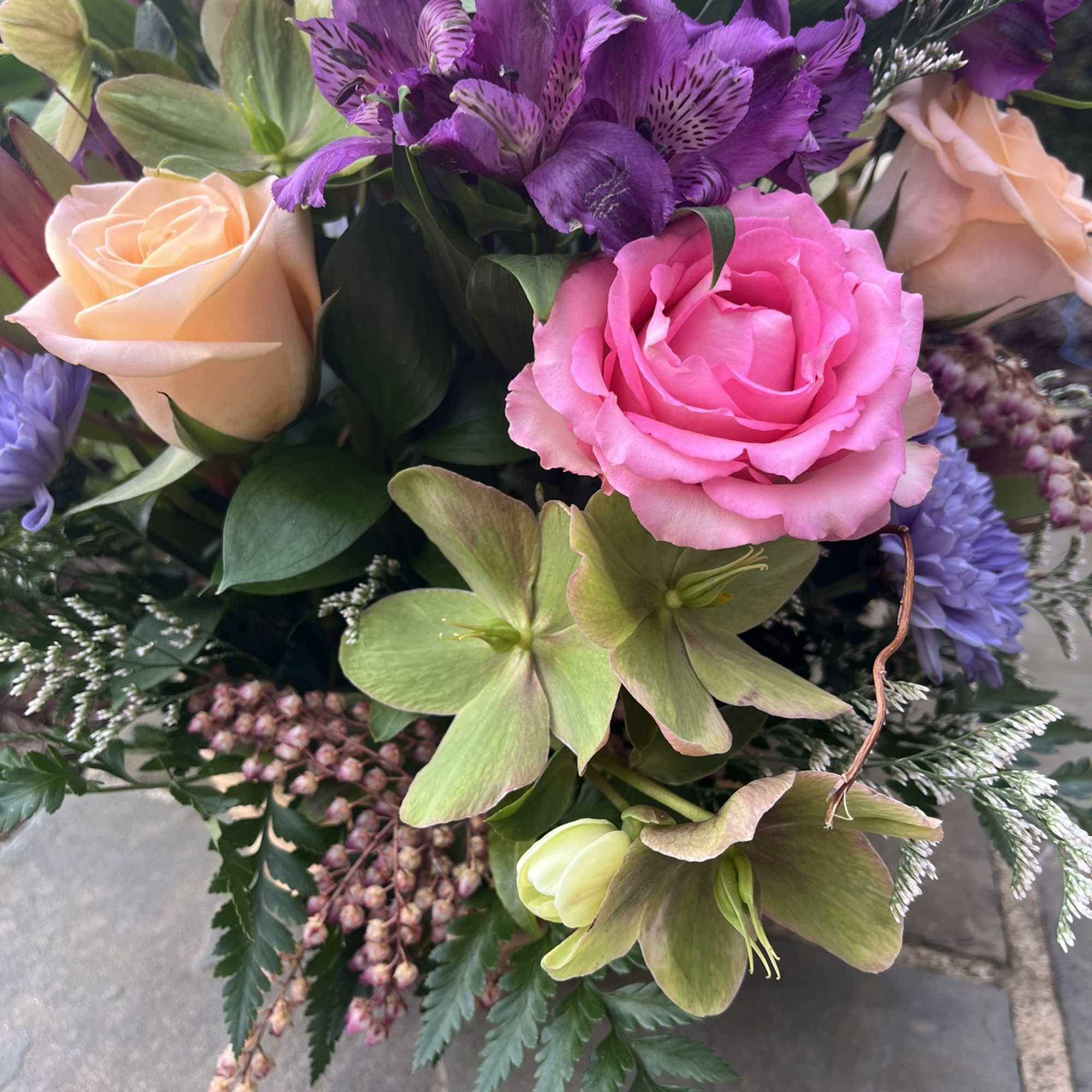 Bouquet of pink and peach roses with purple flowers and green blooms