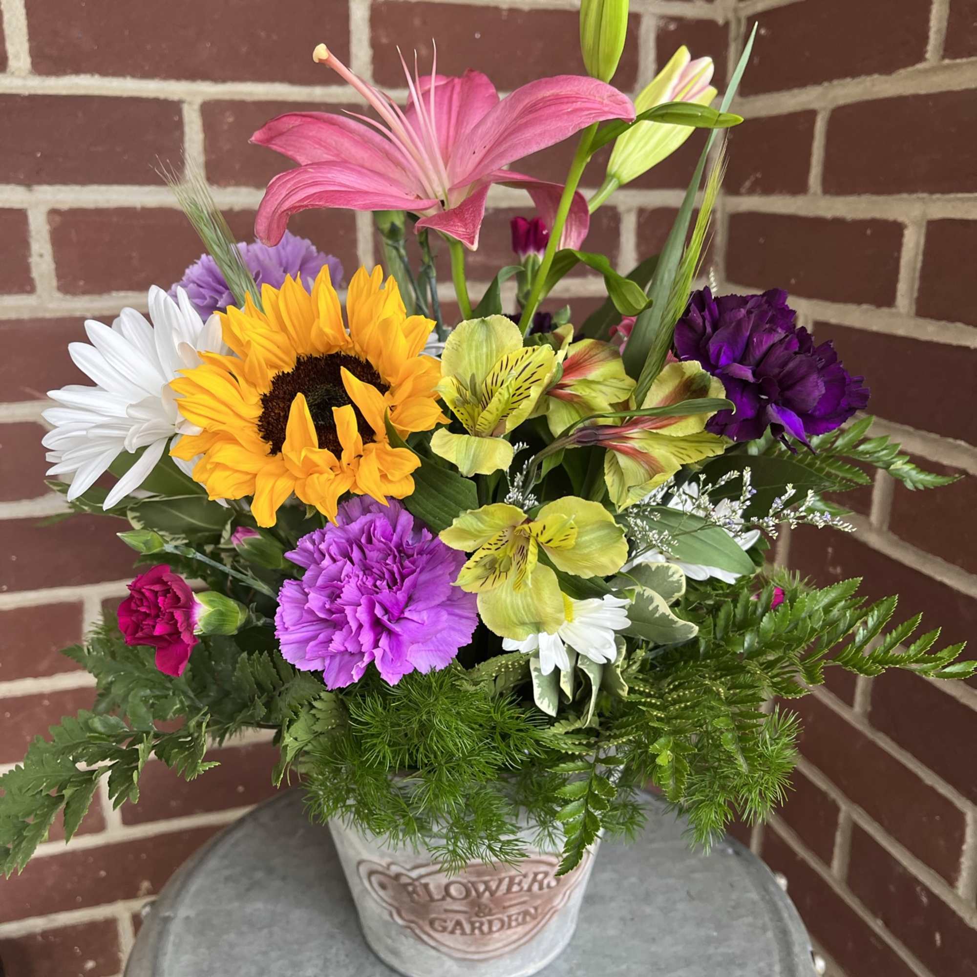 Mixed bouquet in a decorative pot with a pink lily, sunflower, daisies, and carnations