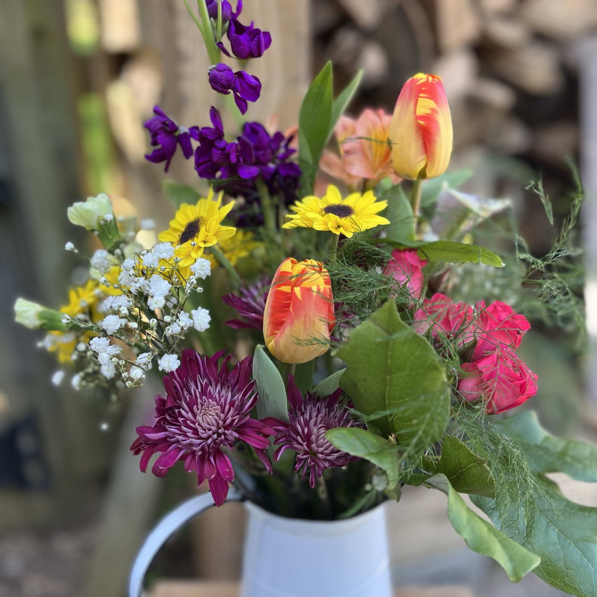 Mixed bouquet with purple, yellow, and pink flowers in a white pitcher vase