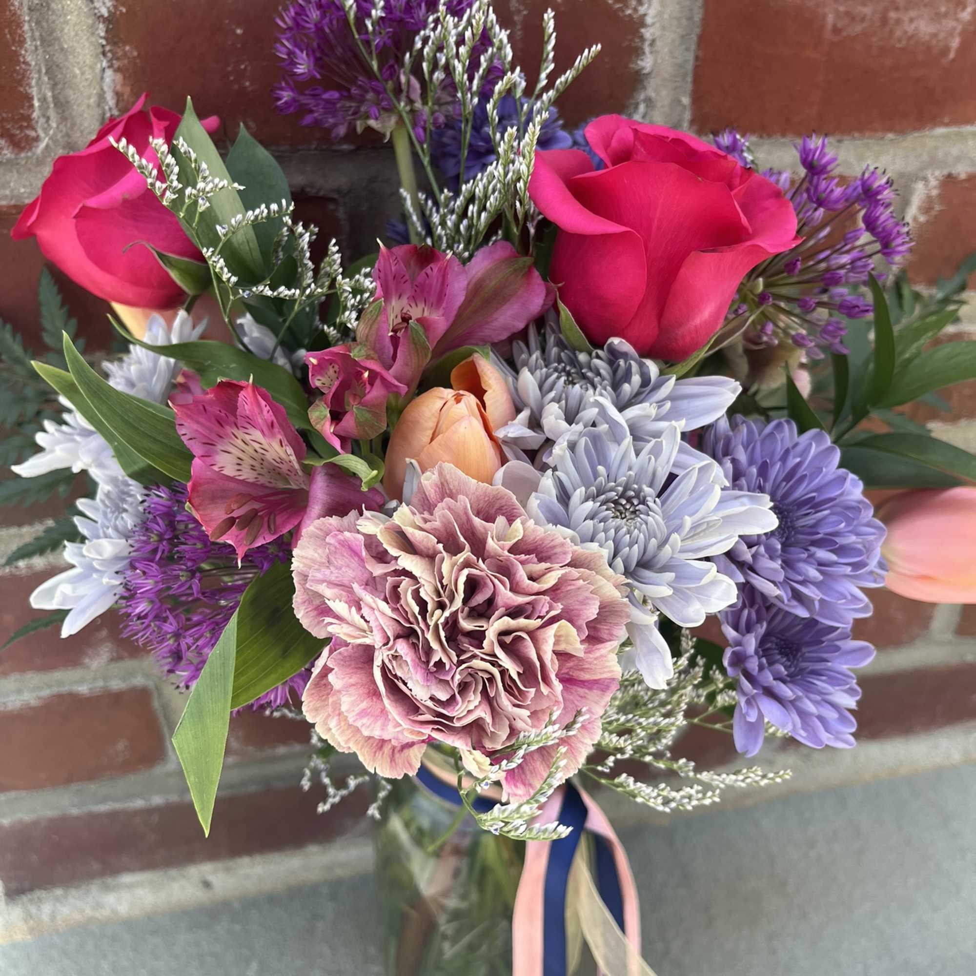 Mixed bouquet of pink roses, carnations, and purple flowers in a glass vase
