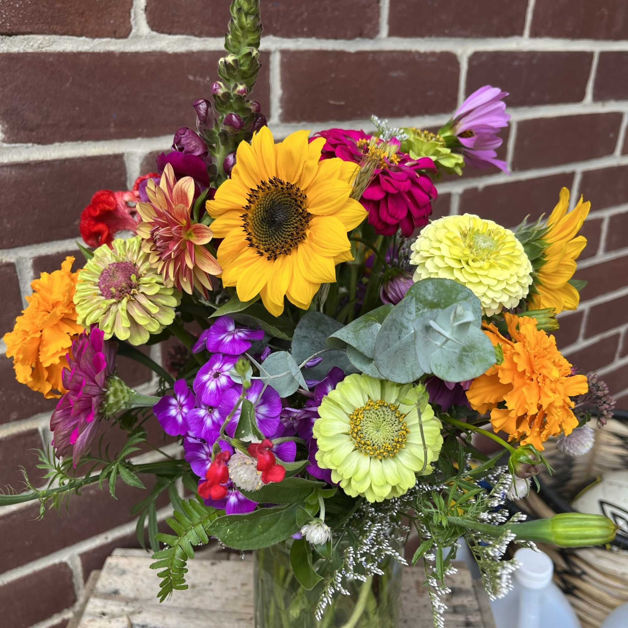 Mixed bouquet with sunflowers, zinnias, and orange marigolds in a glass vase
