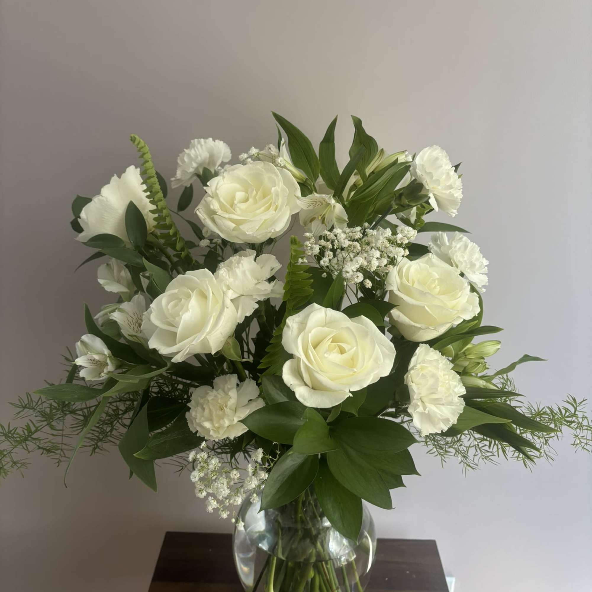 White roses and carnations arranged in a clear glass vase