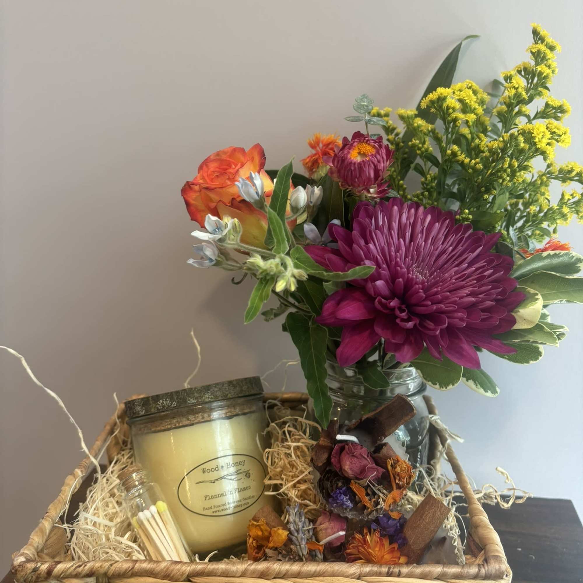 Basket gift set with a flower arrangement, candle, matches, and dried botanicals