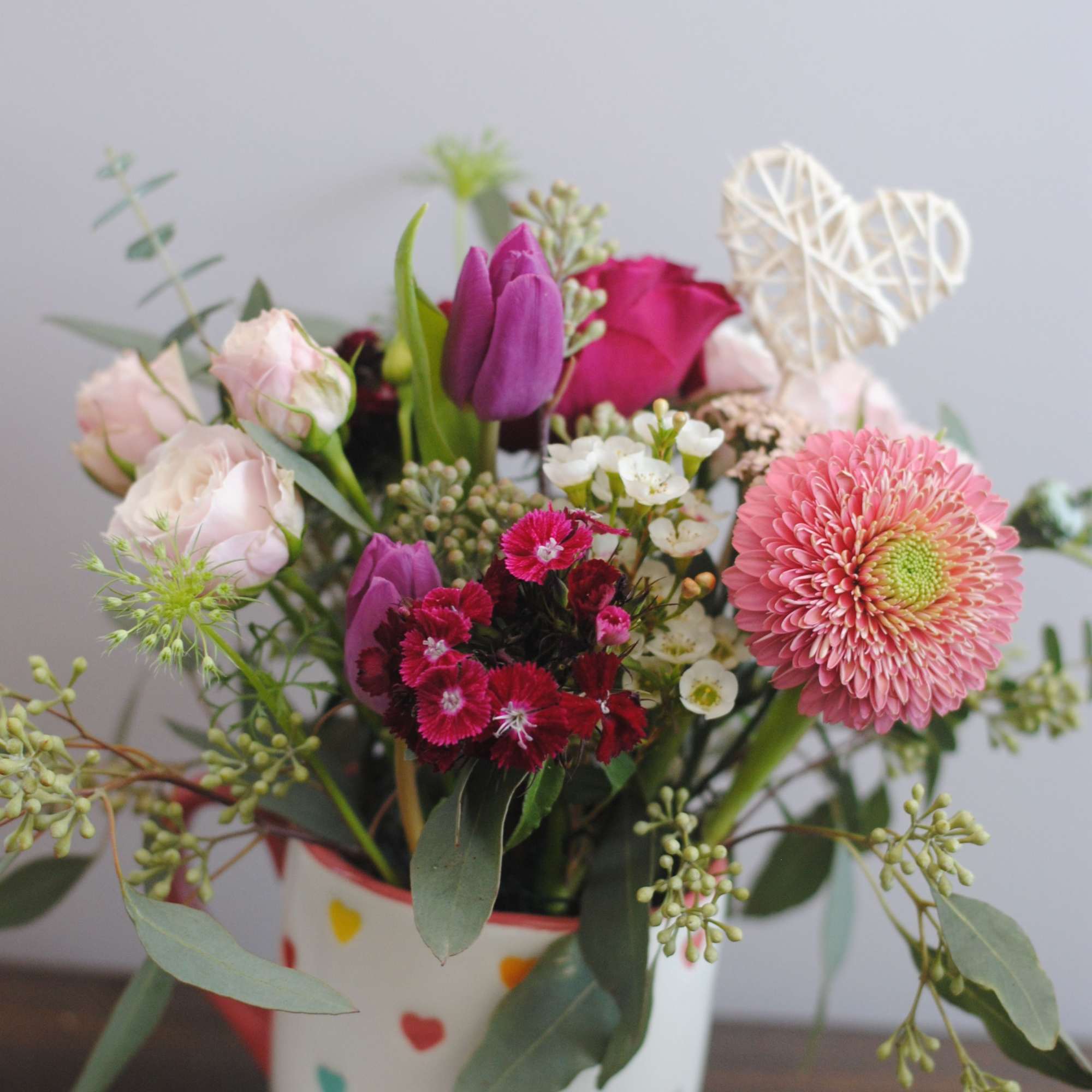 Mixed pink and purple flower arrangement in a heart-patterned mug