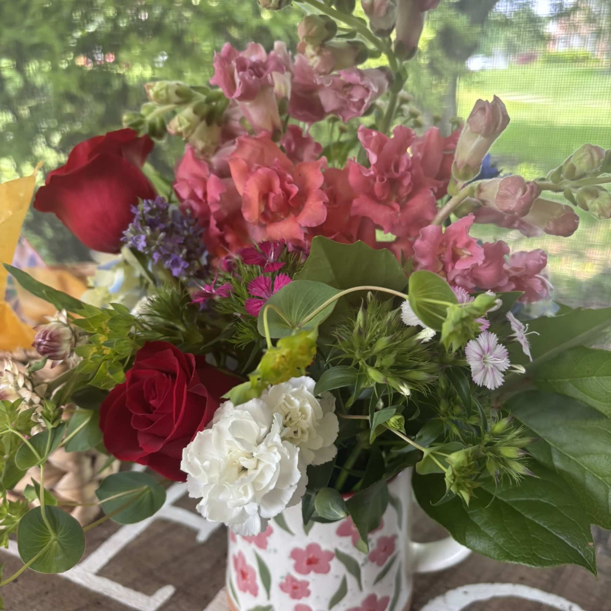 Mixed bouquet of pink snapdragons, red roses, and white carnations in a floral mug