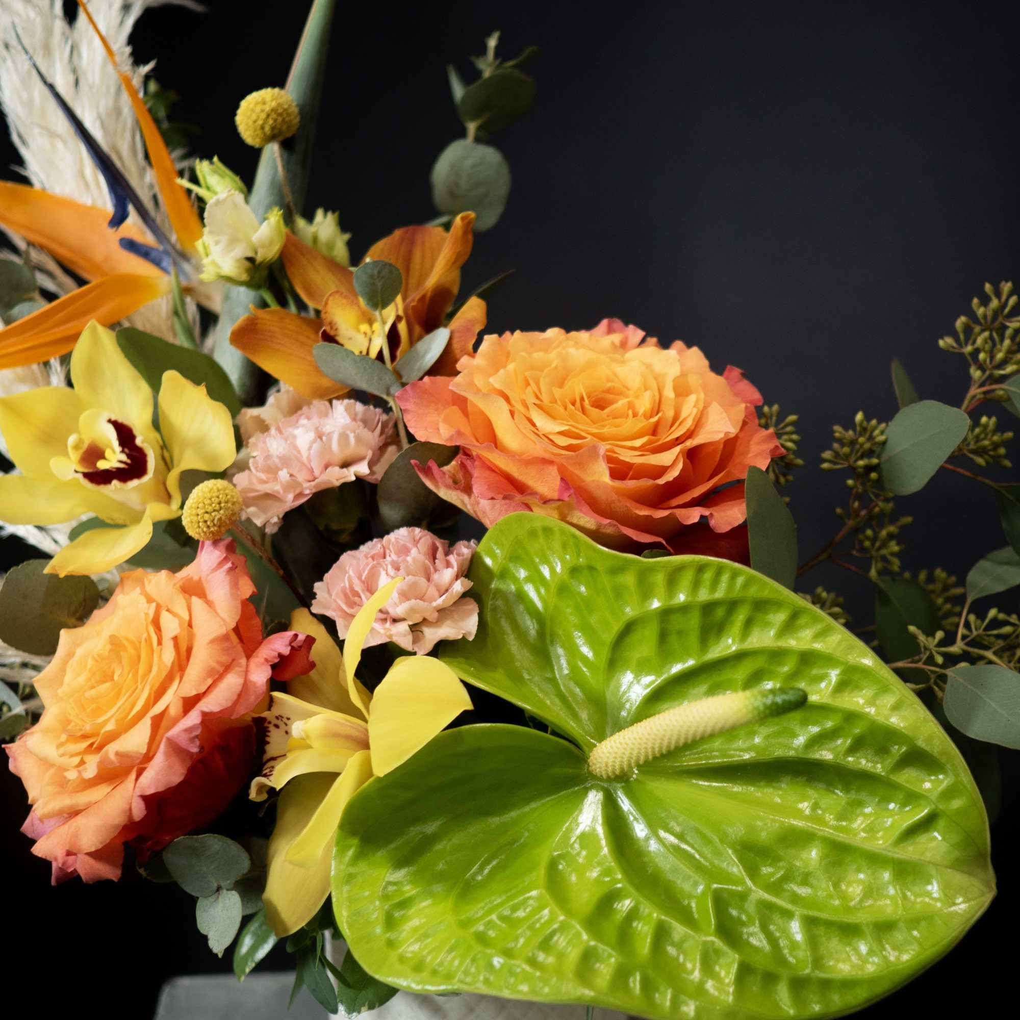 Bright tropical bouquet in a white vase with orange roses and yellow orchids