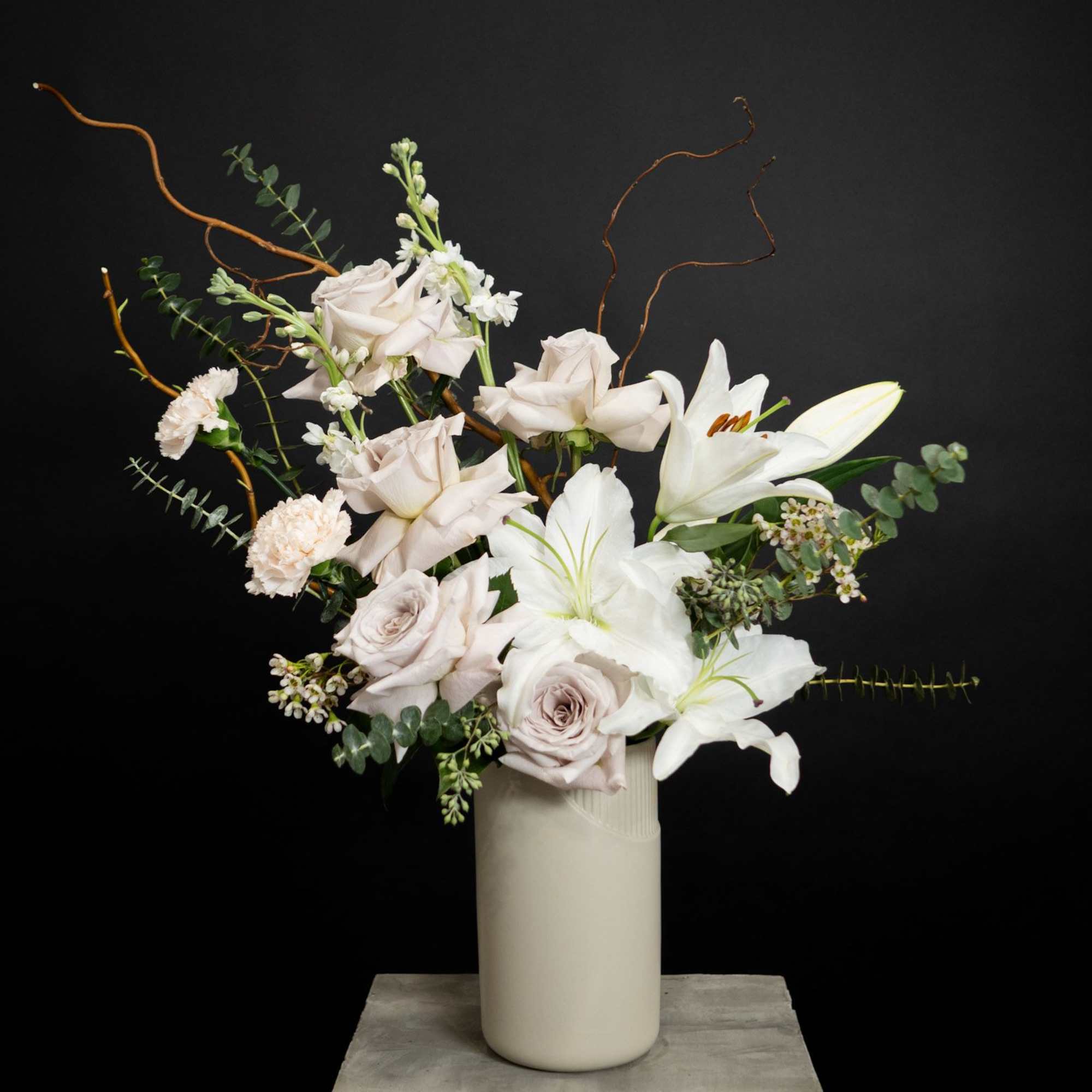 White lilies and pale roses in a tall vase with curly branches