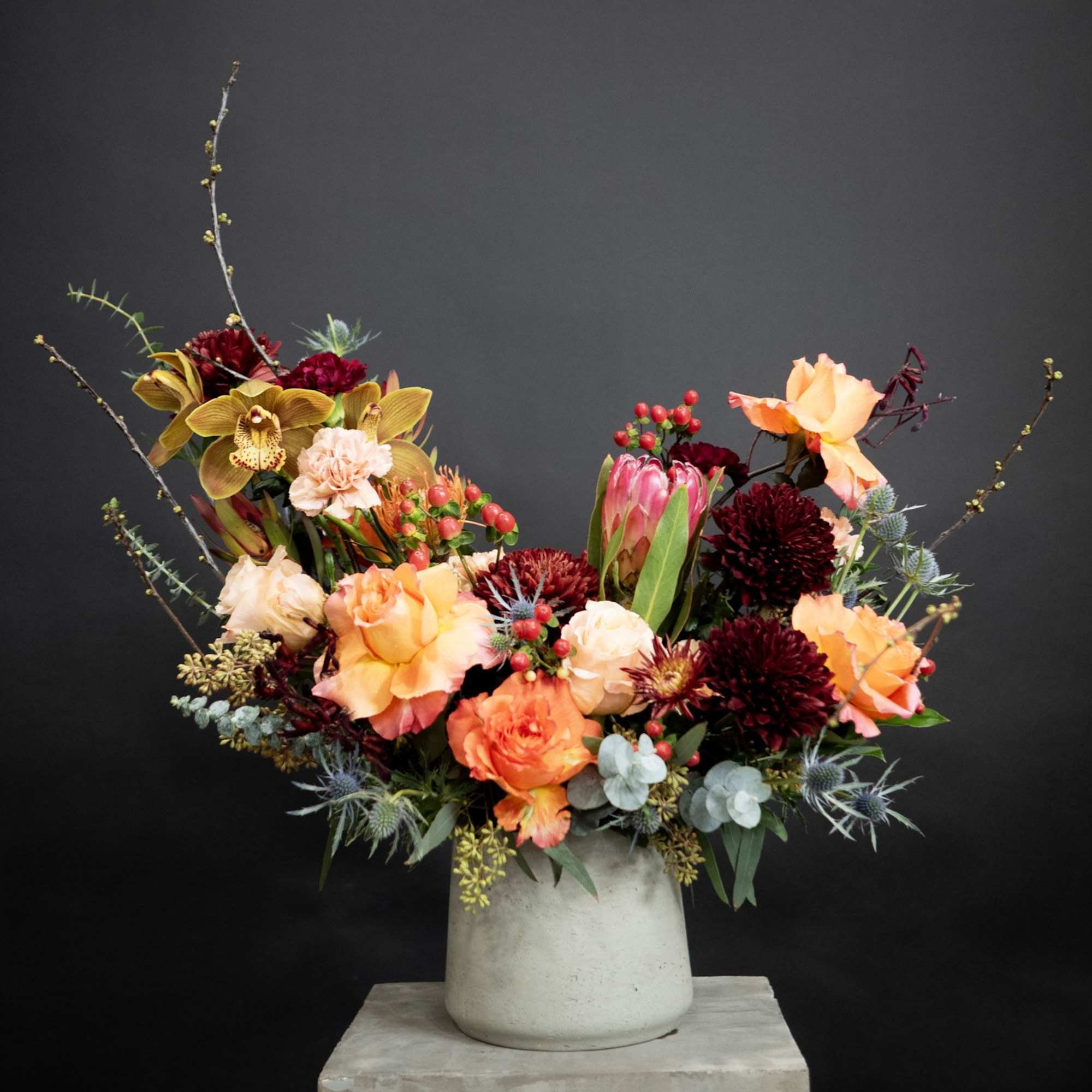 Mixed floral arrangement in a white vase with orange, burgundy, and peach blooms