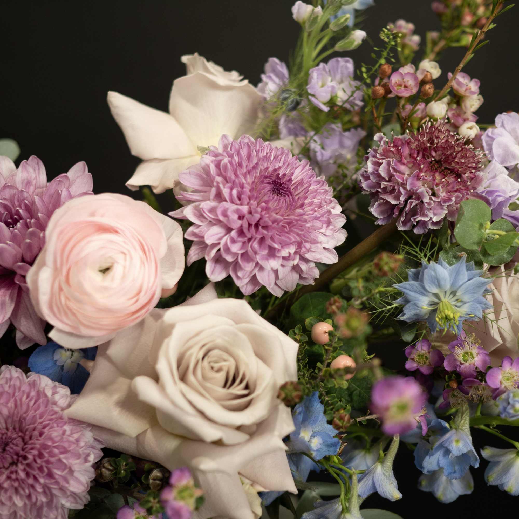 Pastel bouquet with roses, ranunculus, and purple blooms in a white vase