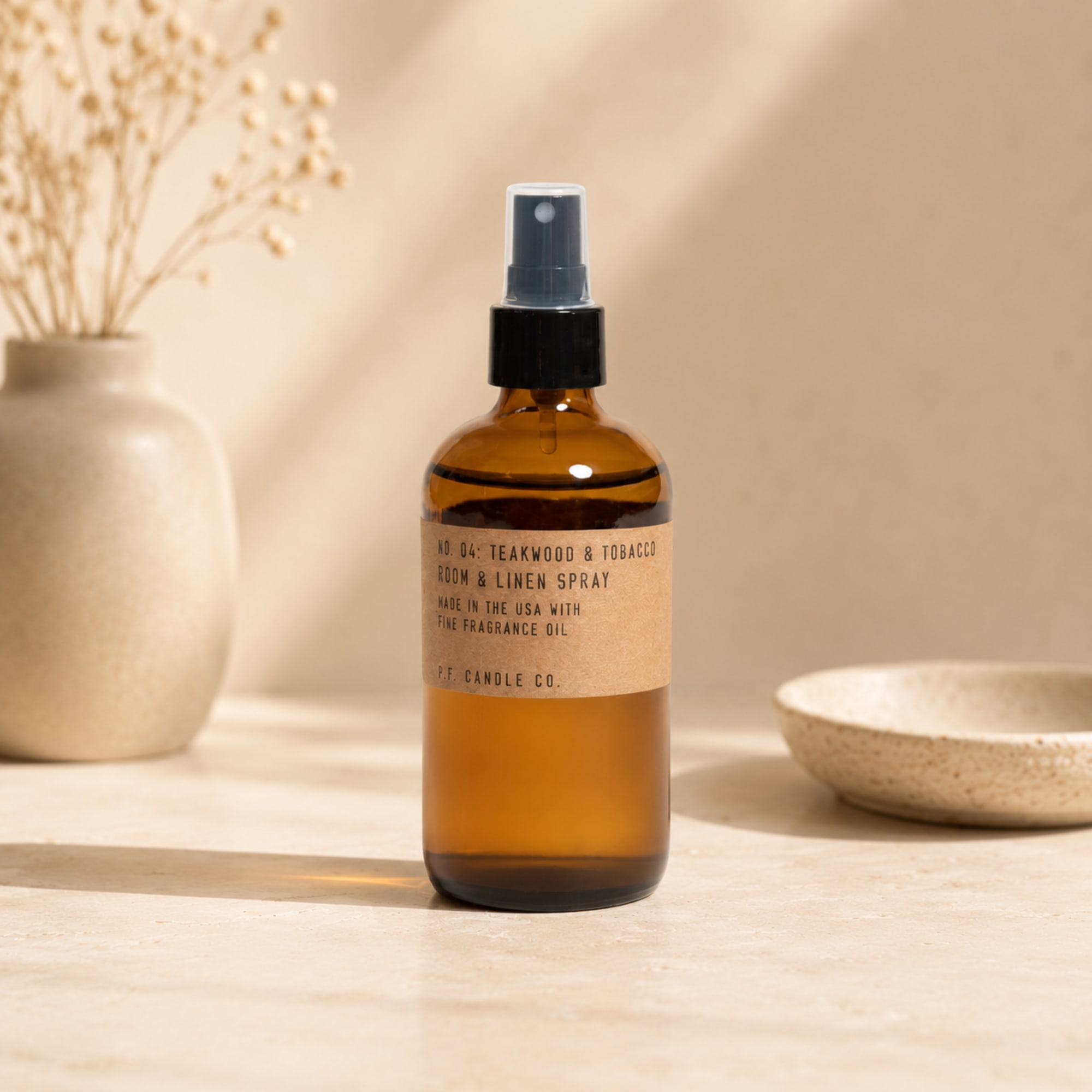 Amber room spray bottle on a neutral tabletop with a vase and bowl nearby