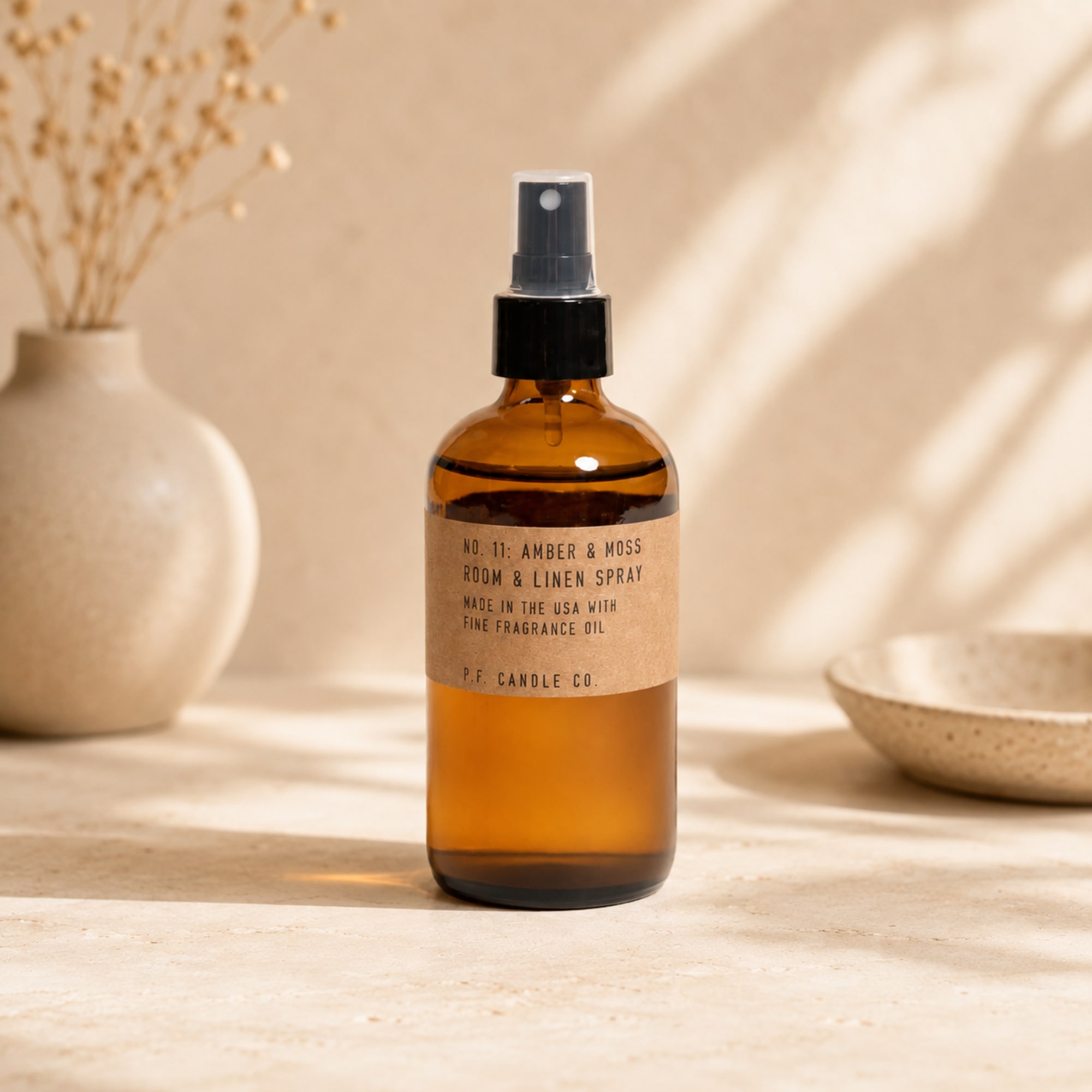 Amber room spray bottle with a black pump on a neutral tabletop