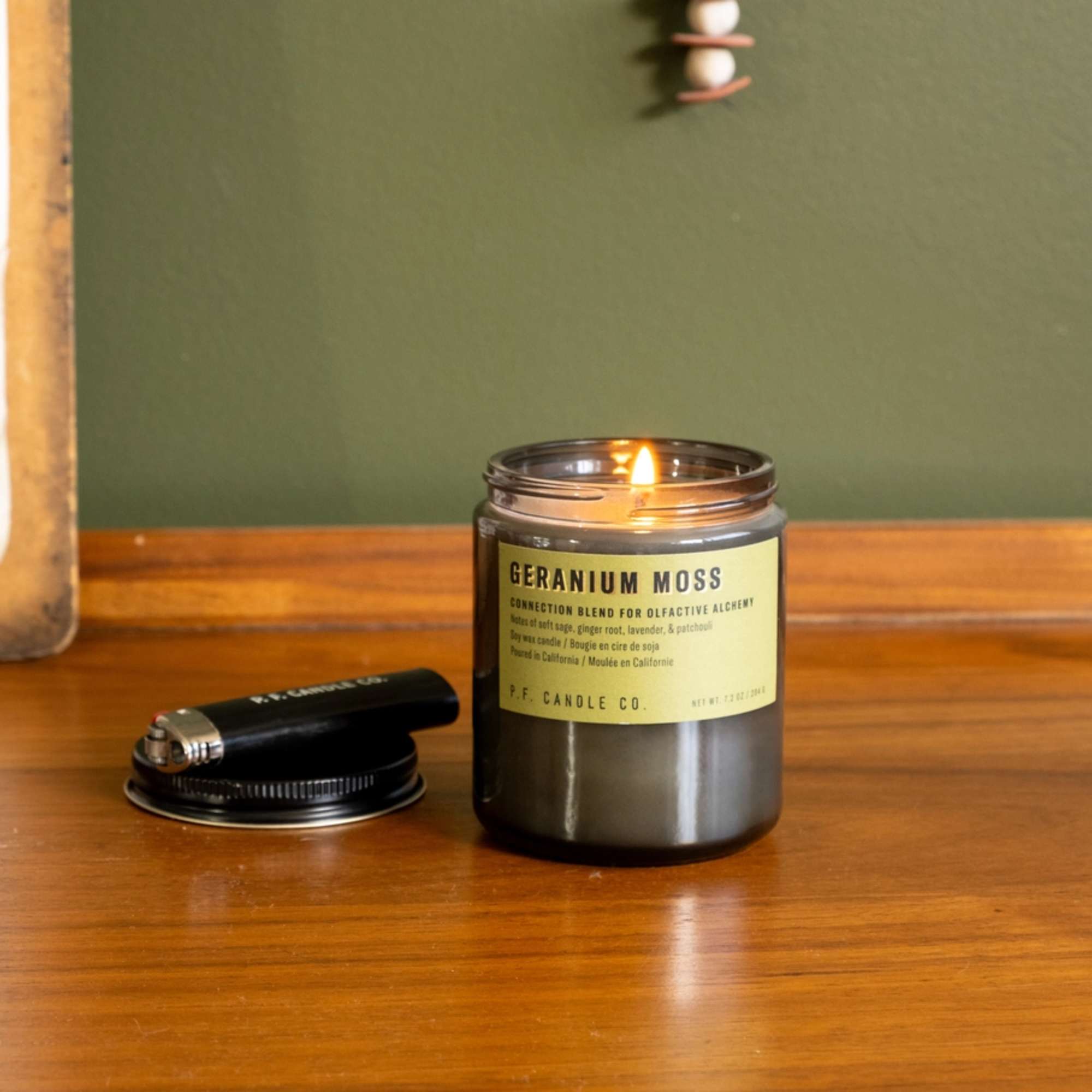 Lit geranium moss candle in a glass jar with a black lid beside it