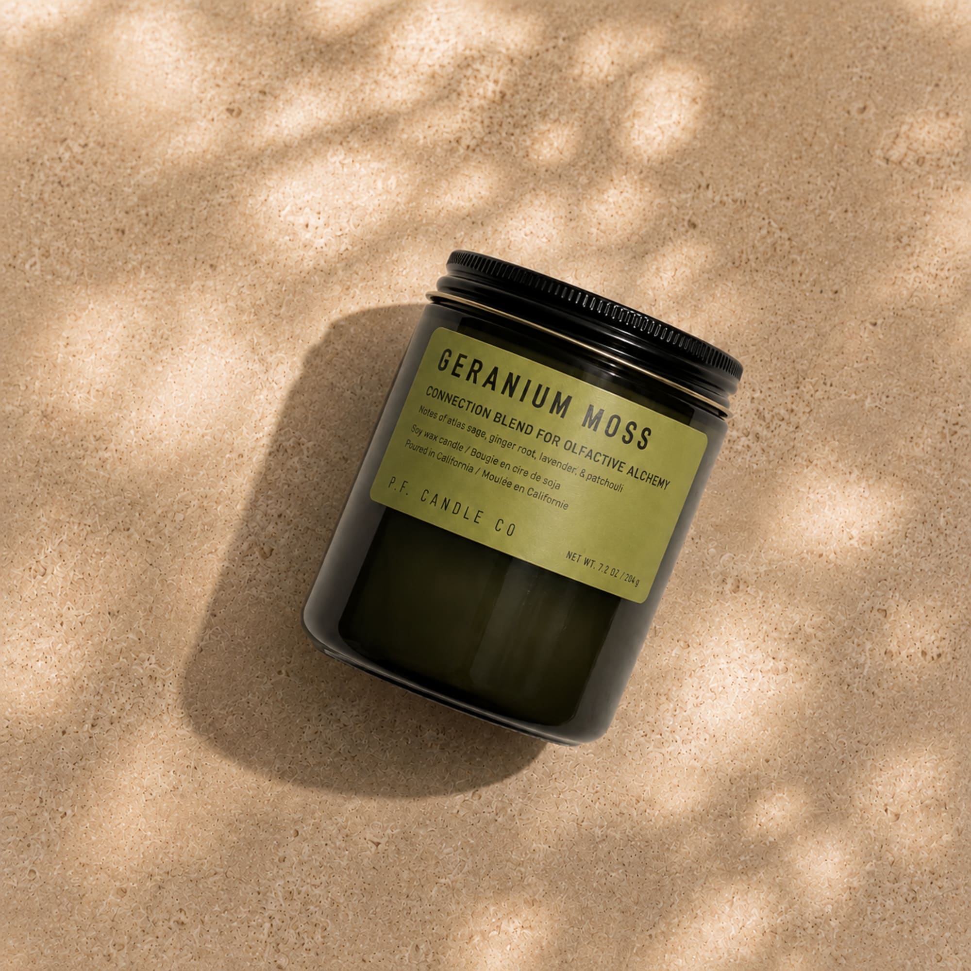 Black jar candle with a green label on a beige surface