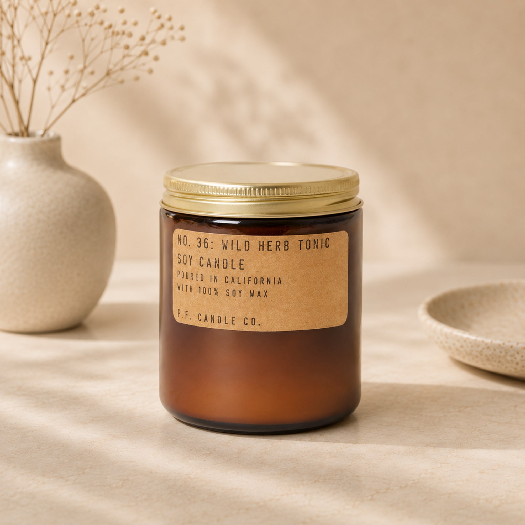 Amber jar candle with a gold lid on a beige surface
